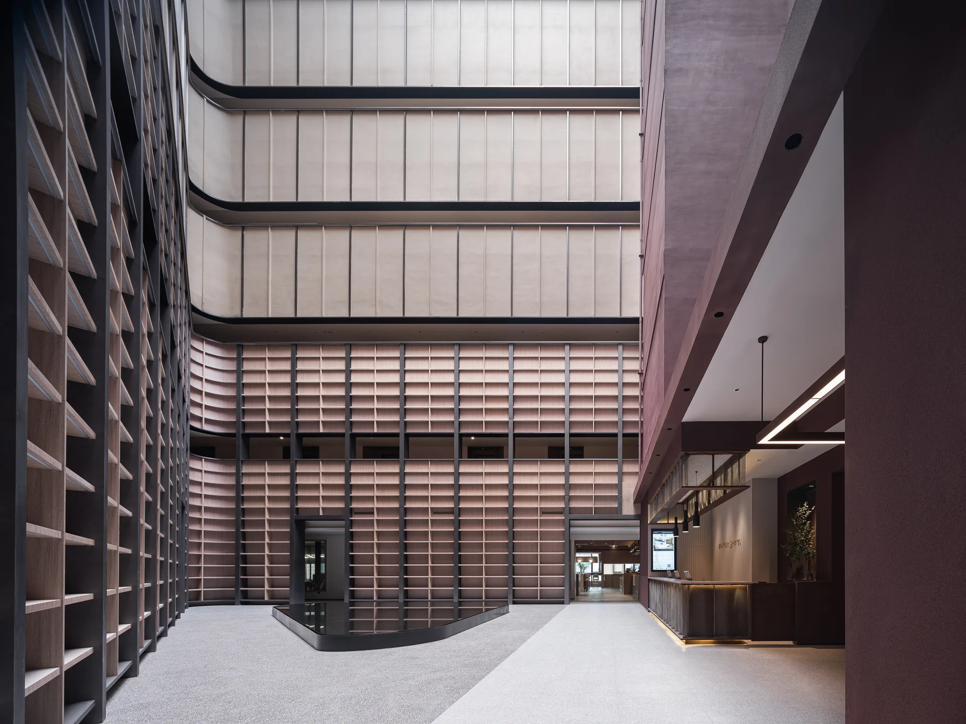 A large hotel lobby atrium features towering wood grid shelving walls, a dark reflecting pool on the stone floor, and a modern reception desk.
