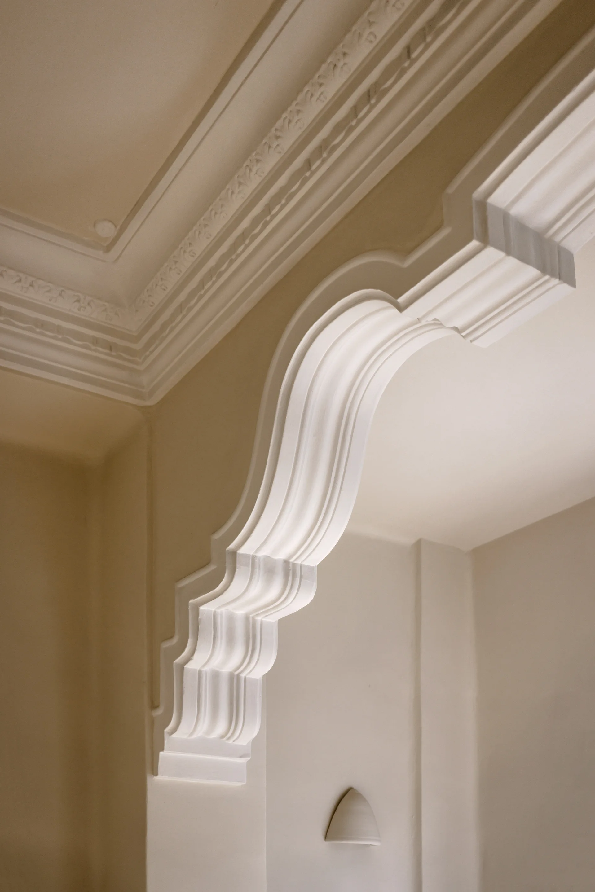 A close-up of a decorative cream plaster archway with ornate curves transitioning into a molded ceiling cornice.