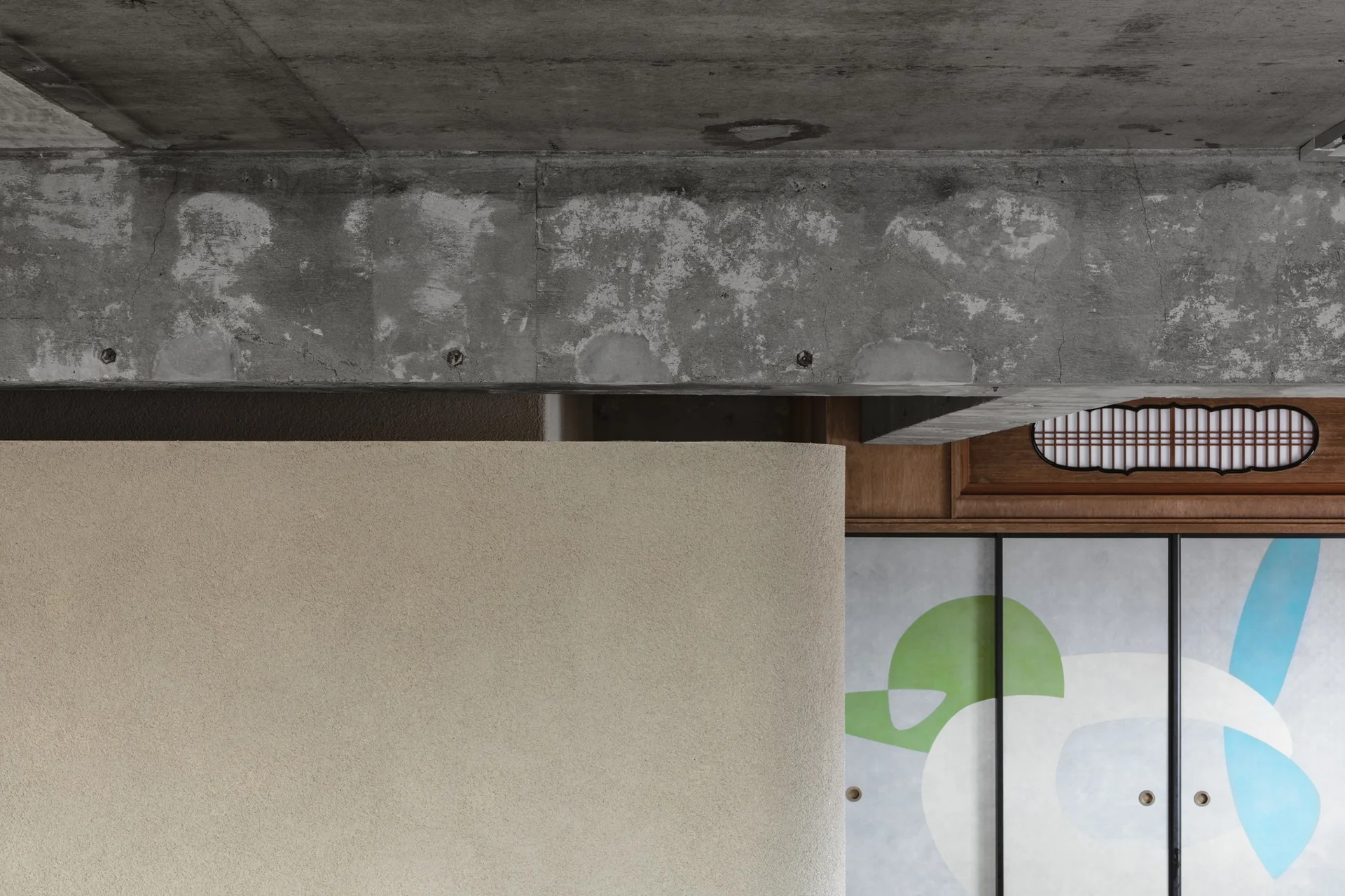 An exposed concrete ceiling beam sits above a textured beige plaster wall and a traditional wooden transom window with a decorative sliding door.