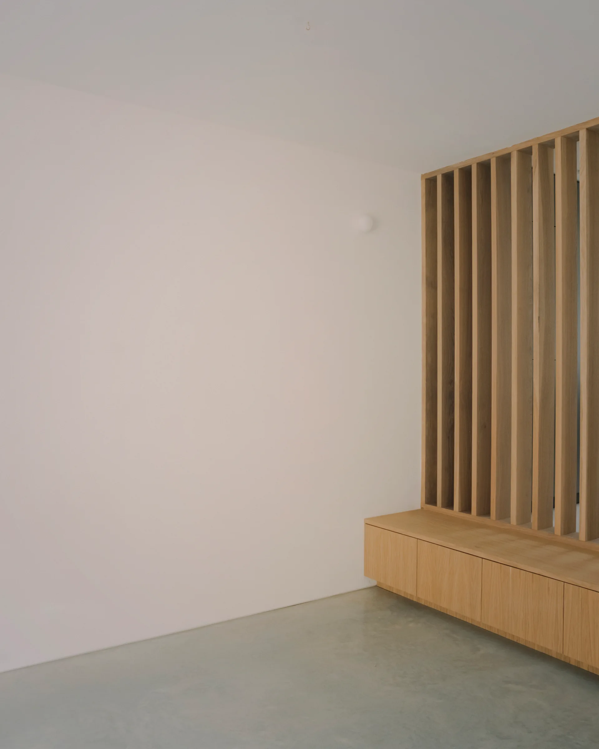 A low built-in wooden cabinet with a vertical slatted partition screen stands on a polished concrete floor against a white wall.