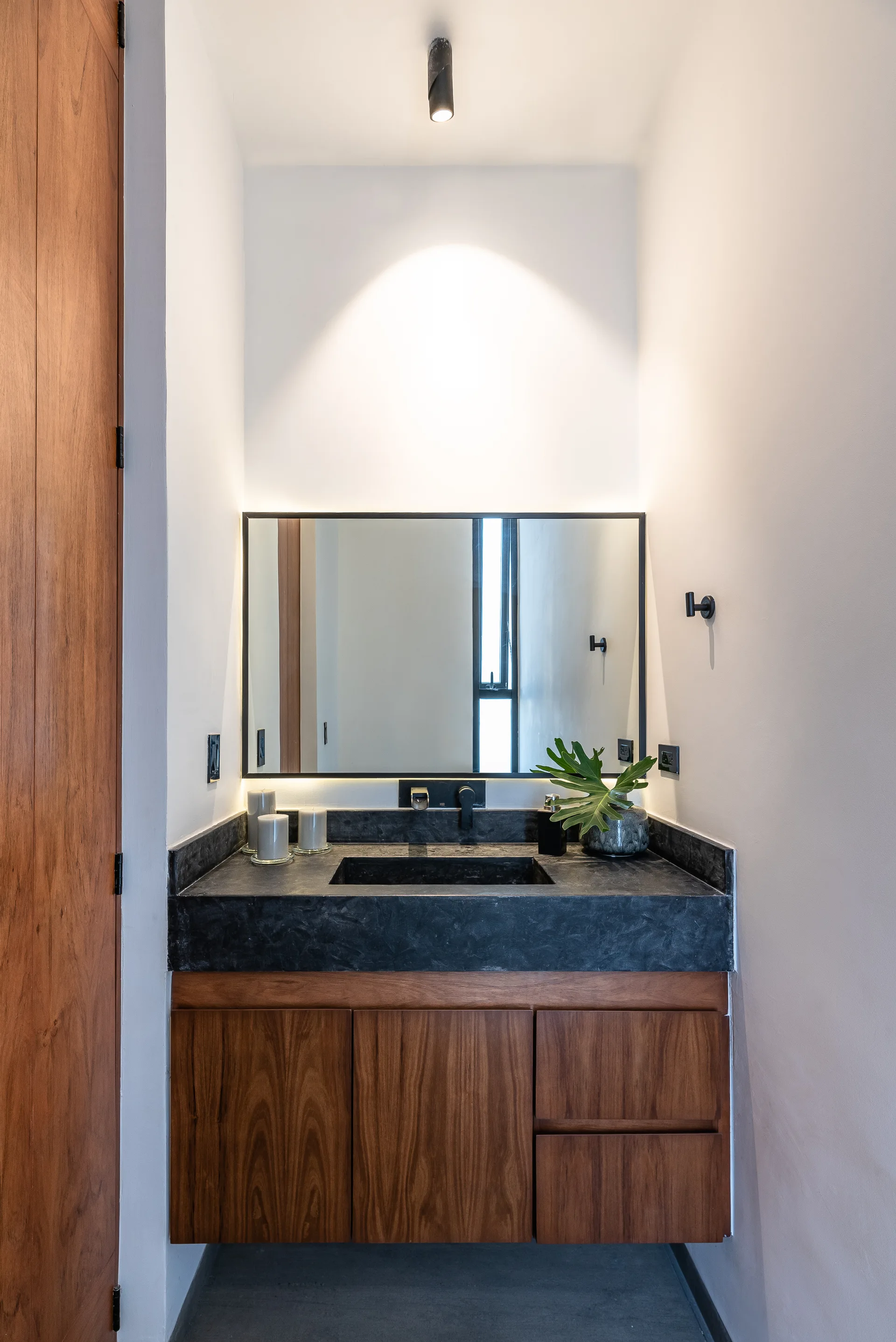 A modern bathroom alcove features a floating wood vanity with a dark stone countertop, integrated sink, and a backlit rectangular mirror.