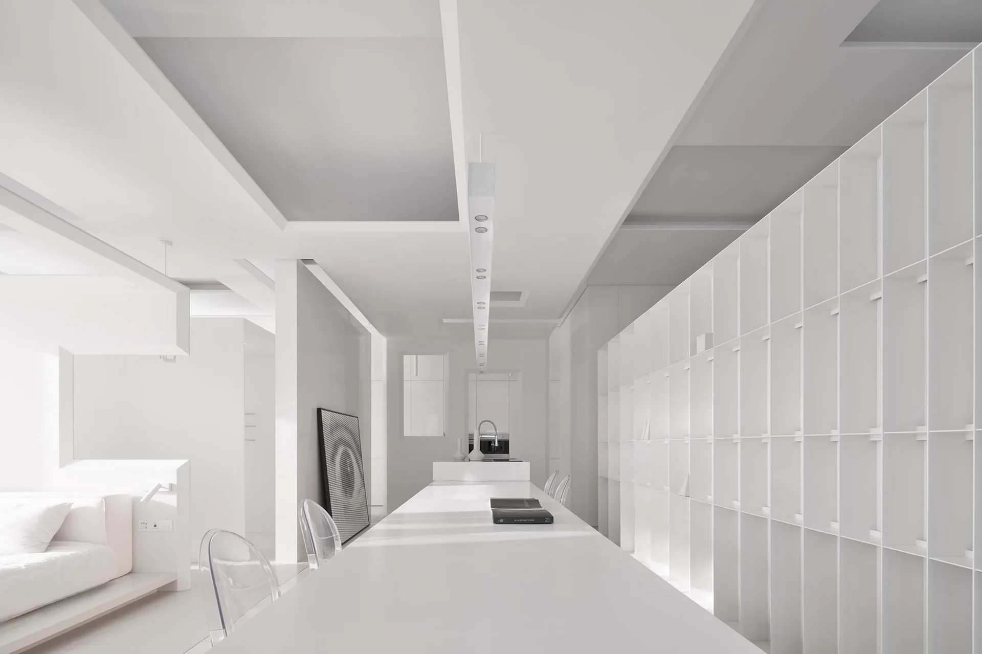 A monochromatic white dining space features a long minimalist table paired with transparent ghost chairs under a linear pendant light.