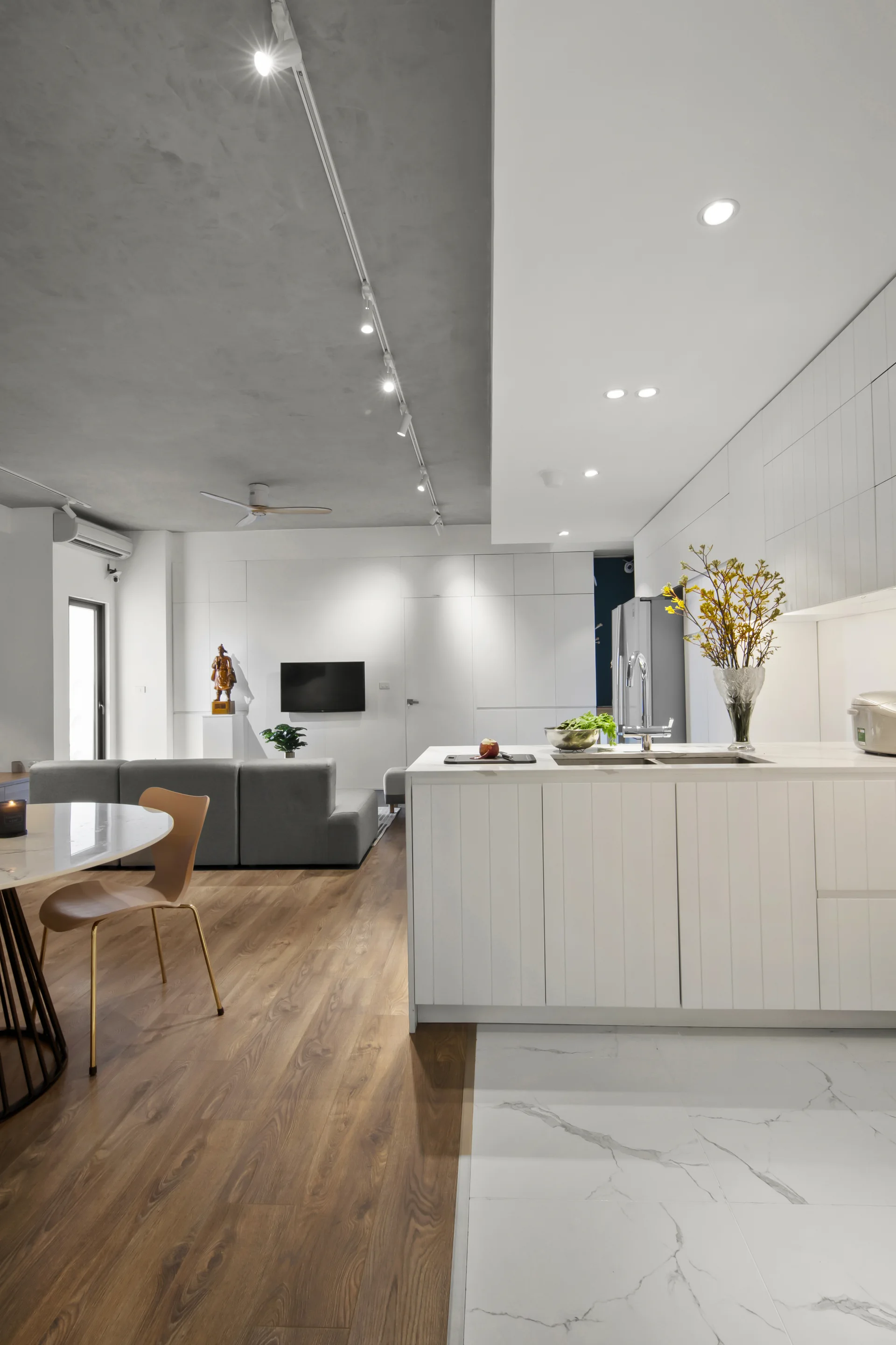 An open concept kitchen and living area showing white tile floor transitioning to wood planks under a two tone grey and white ceiling.