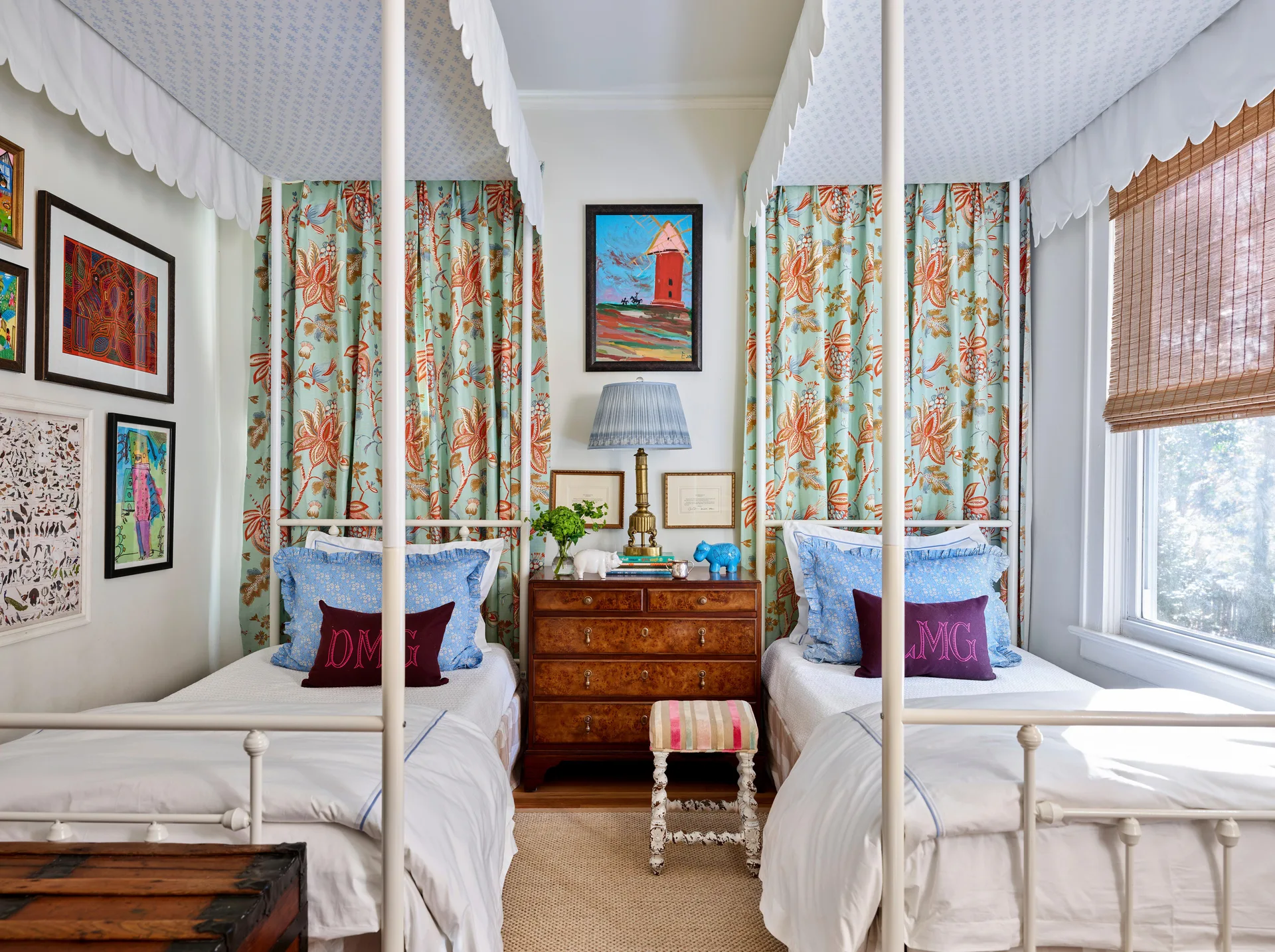 Two white twin canopy beds with scalloped valances flank a burl wood dresser beneath framed artwork and floral curtains.