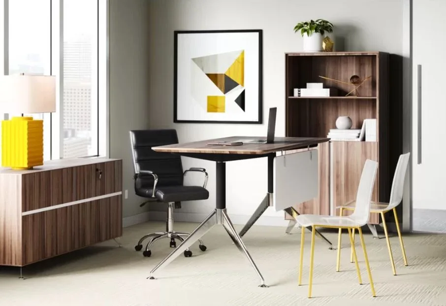A contemporary home office featuring a wood-topped desk, a black leather chair, two clear plastic chairs, and a bright yellow table lamp.