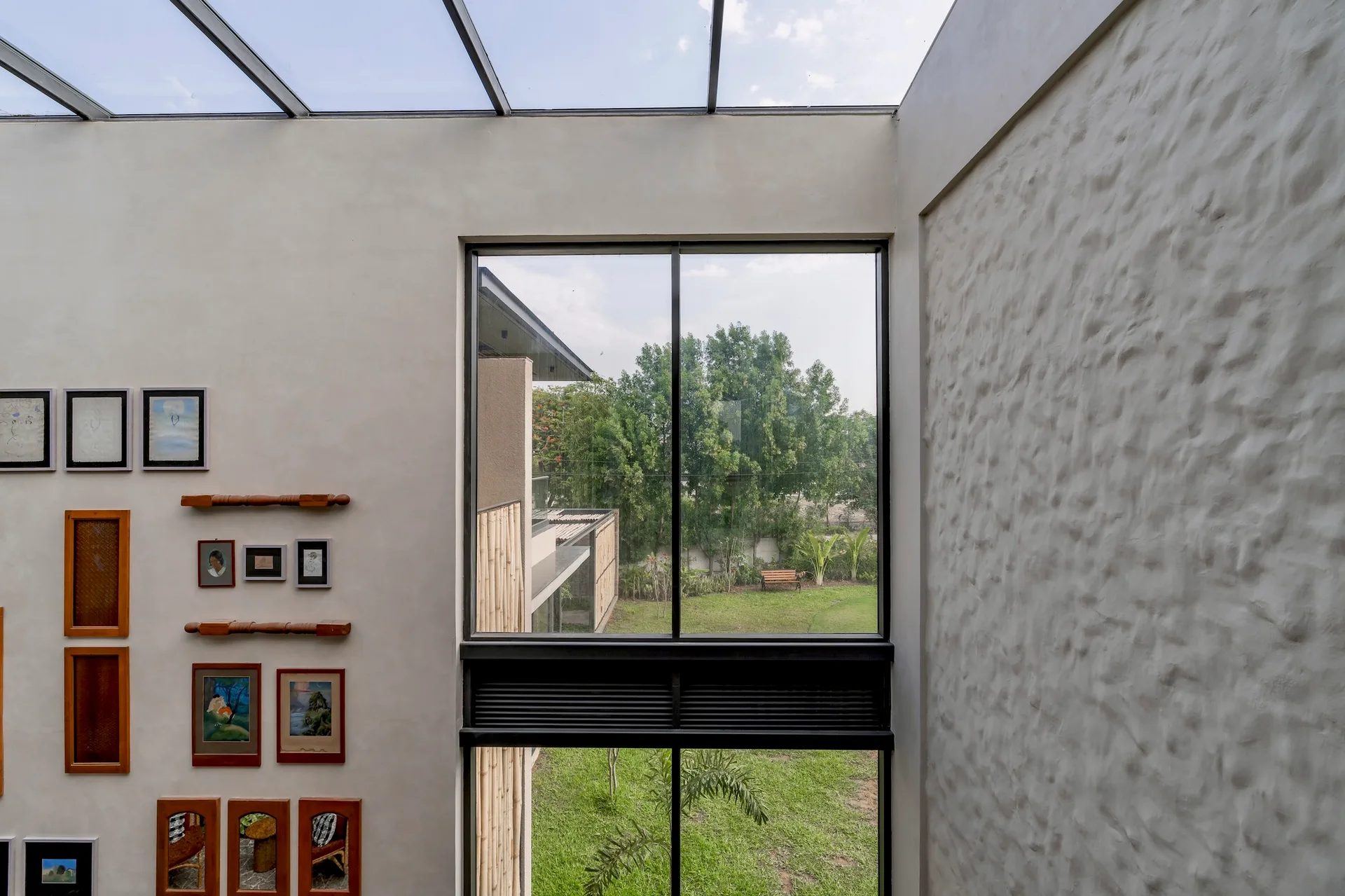 A high-ceiling interior space features a large black-framed picture window, a glass skylight roof, and a textured stucco wall.