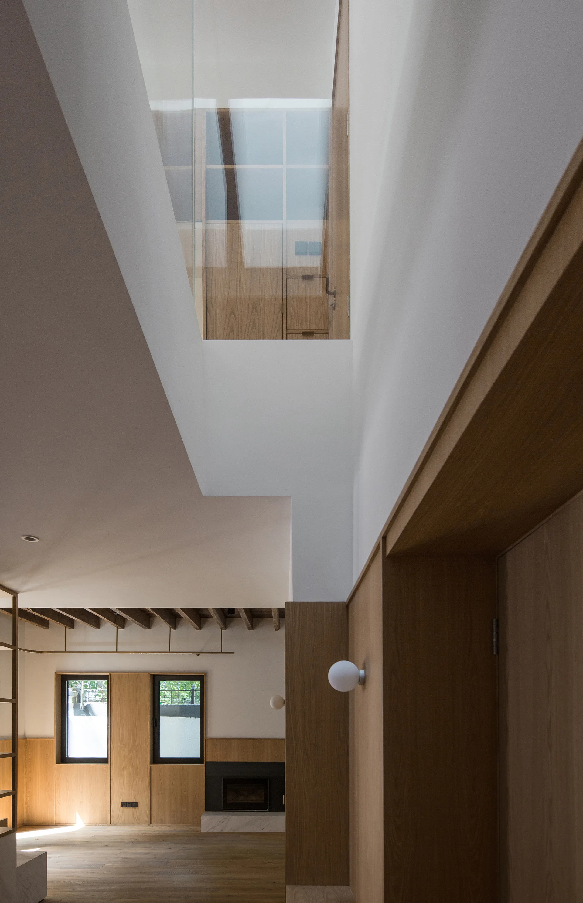 A minimalist living room features wood wall paneling, a fireplace, and a double-height ceiling opening with glass partitions.