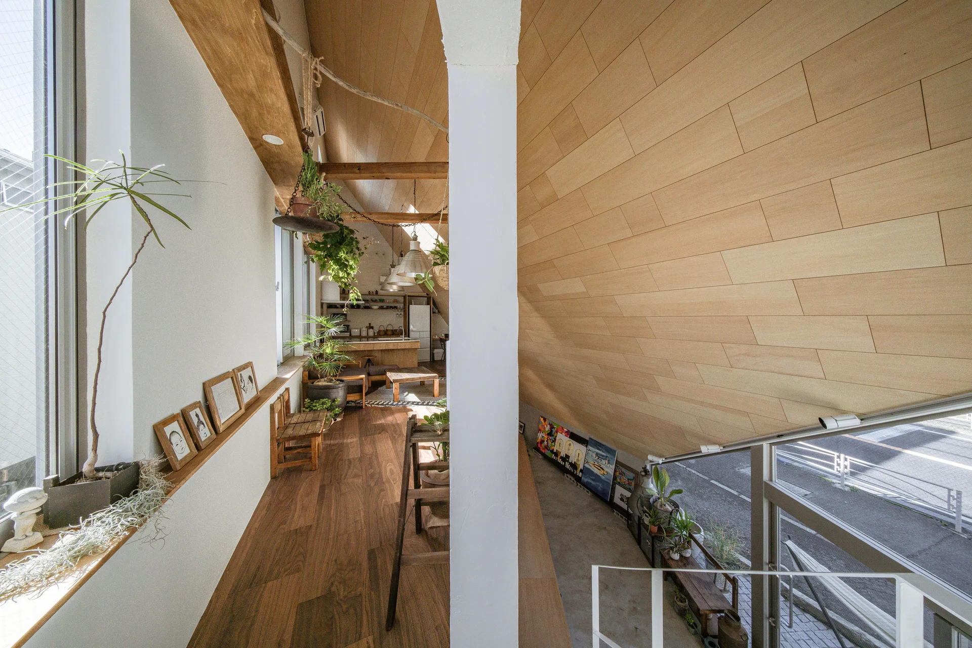 A modern split-level loft interior featuring a sharply sloped wood-plank ceiling, wood floors, and plants near a white structural column.