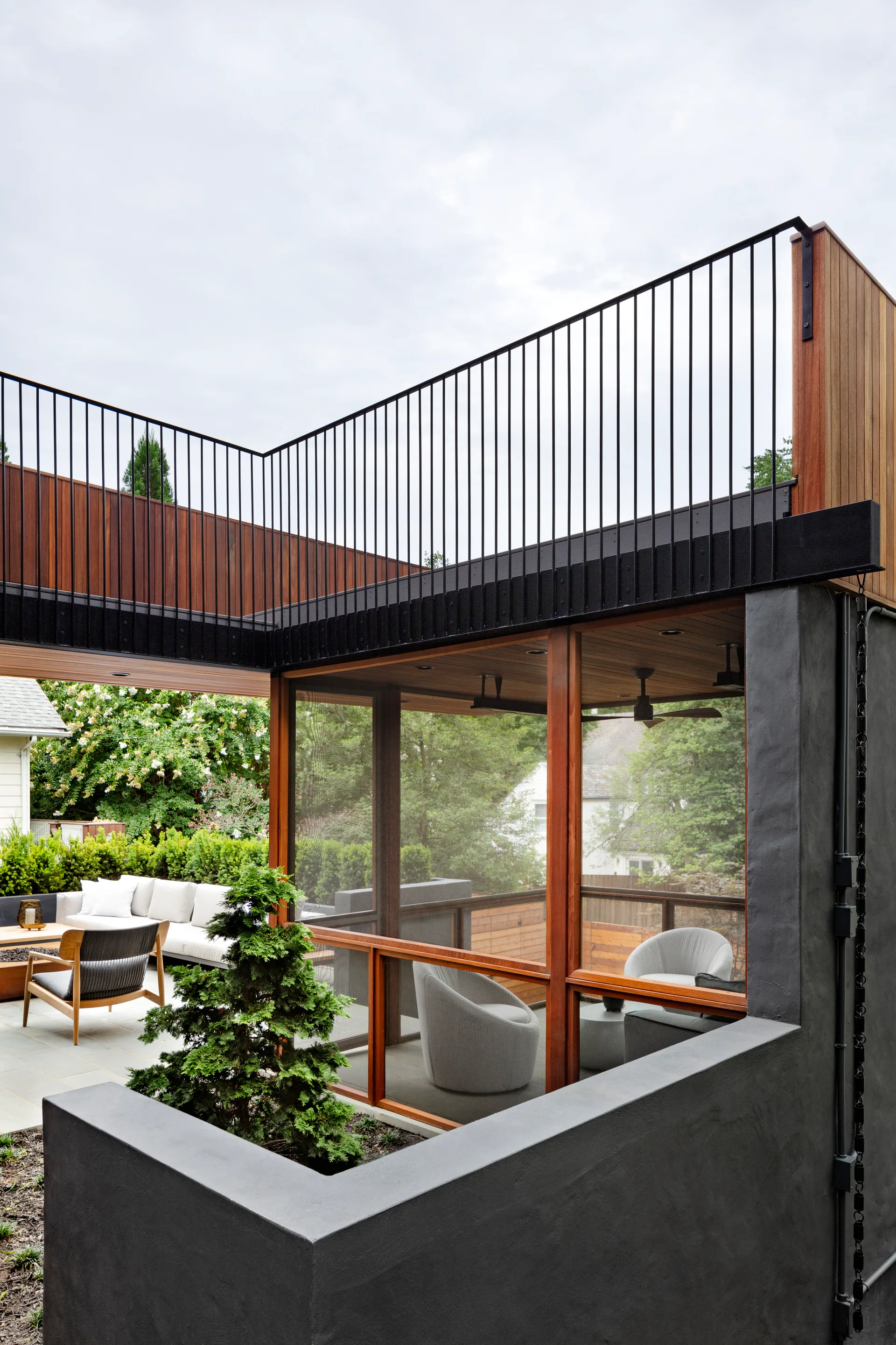 A modern patio with a built-in concrete planter next to a wood-framed screened-in porch and an upper-level deck with black metal railings.