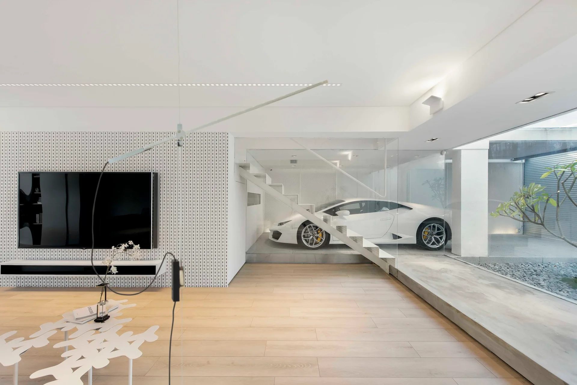 A minimalist living room with light wood floors, a white patterned feature wall, and a glass-walled garage display featuring a white sports car.