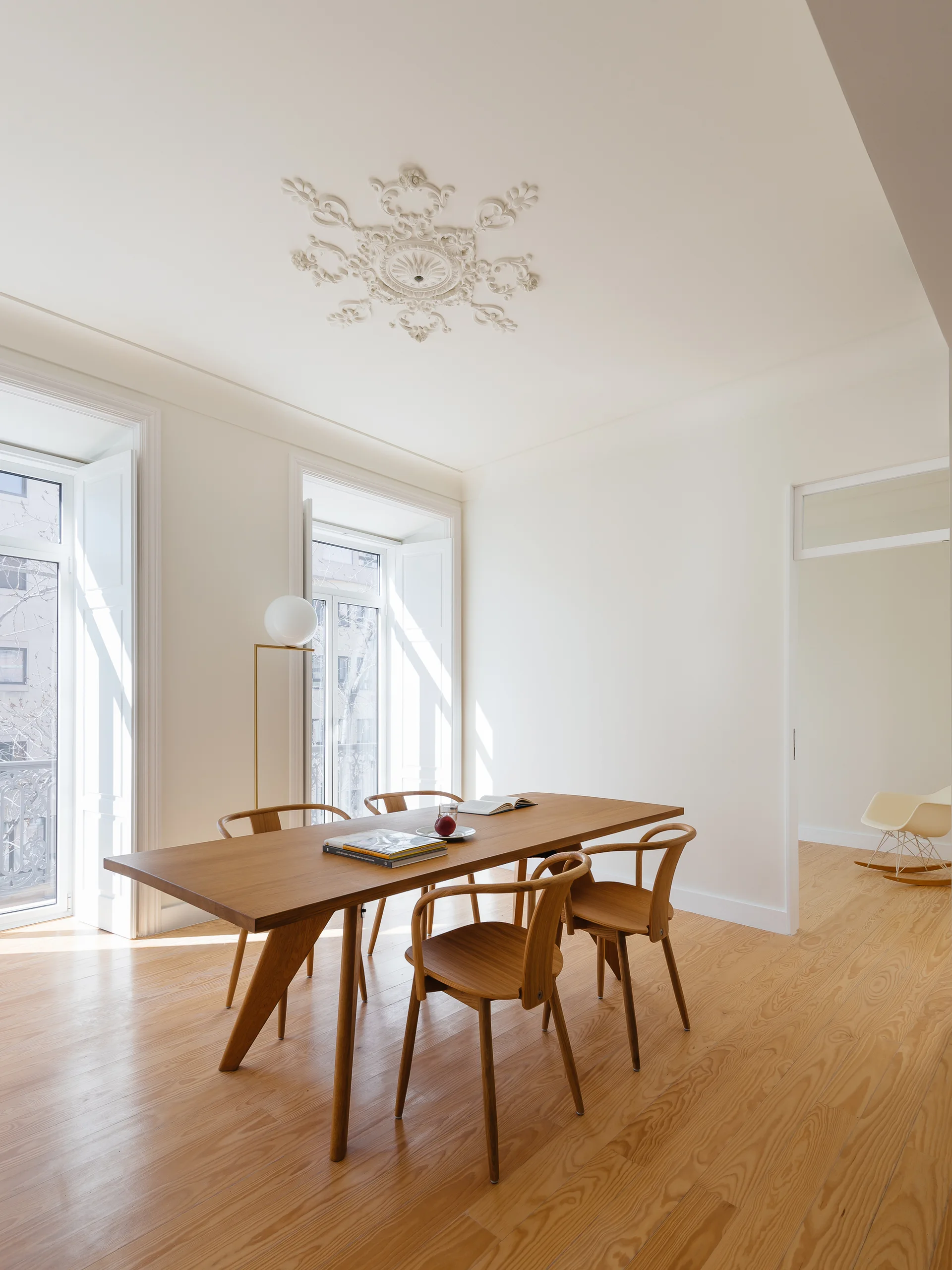 A minimalist dining room features a light wood table and chairs on wood flooring beneath an ornate white plaster ceiling medallion.