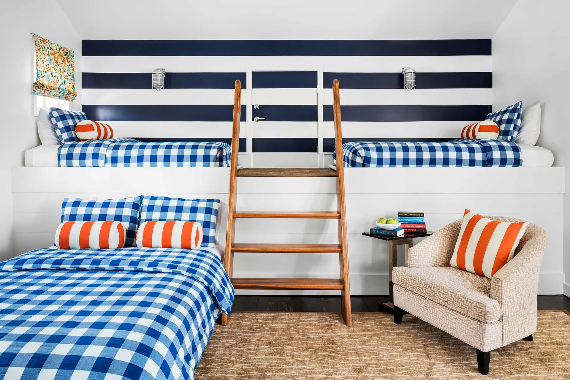 A children's bunk room with navy and white striped walls, built-in beds with blue plaid bedding, and a central wooden ladder.