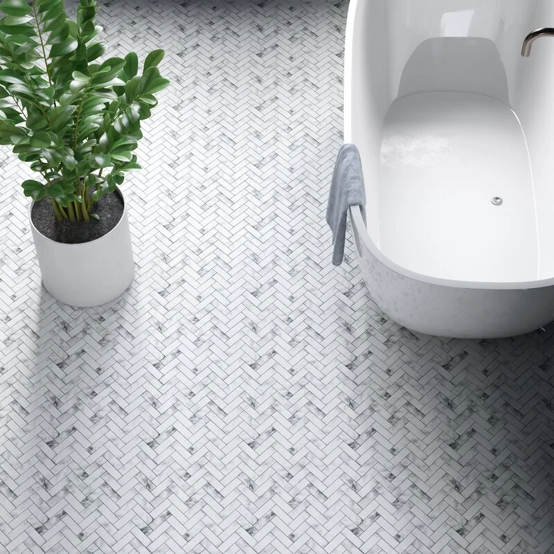 A top-down view of a white freestanding bathtub and a potted green plant on a grey and white marble herringbone tile floor.