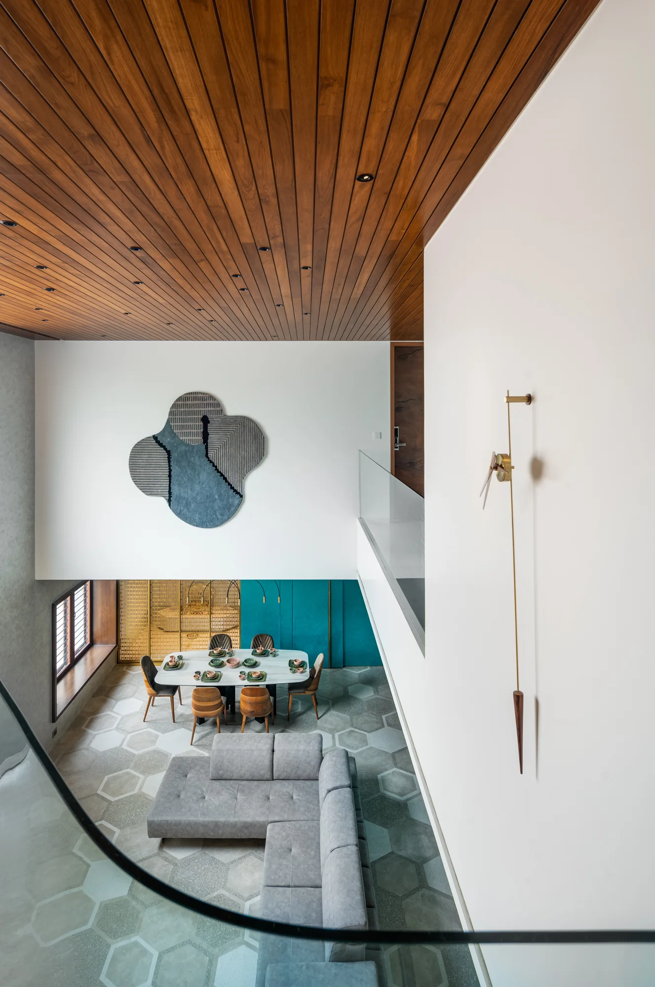 High-angle view of a modern living room featuring a grey sectional sofa, hexagonal floor tiles, and a rich wood-slatted ceiling.