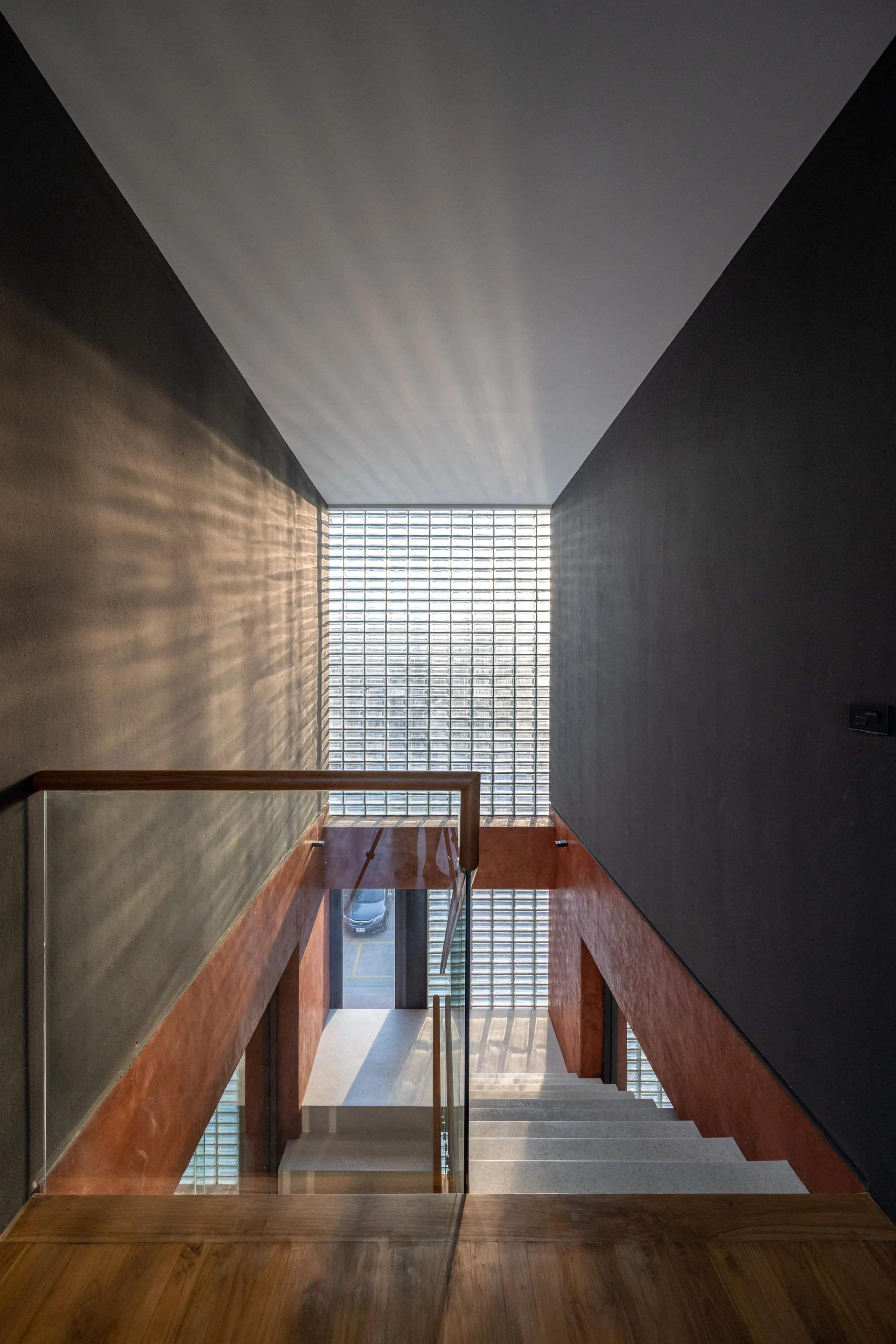A modern stairwell with light gray stone steps features a glass block wall and two-tone charcoal and terracotta painted walls.