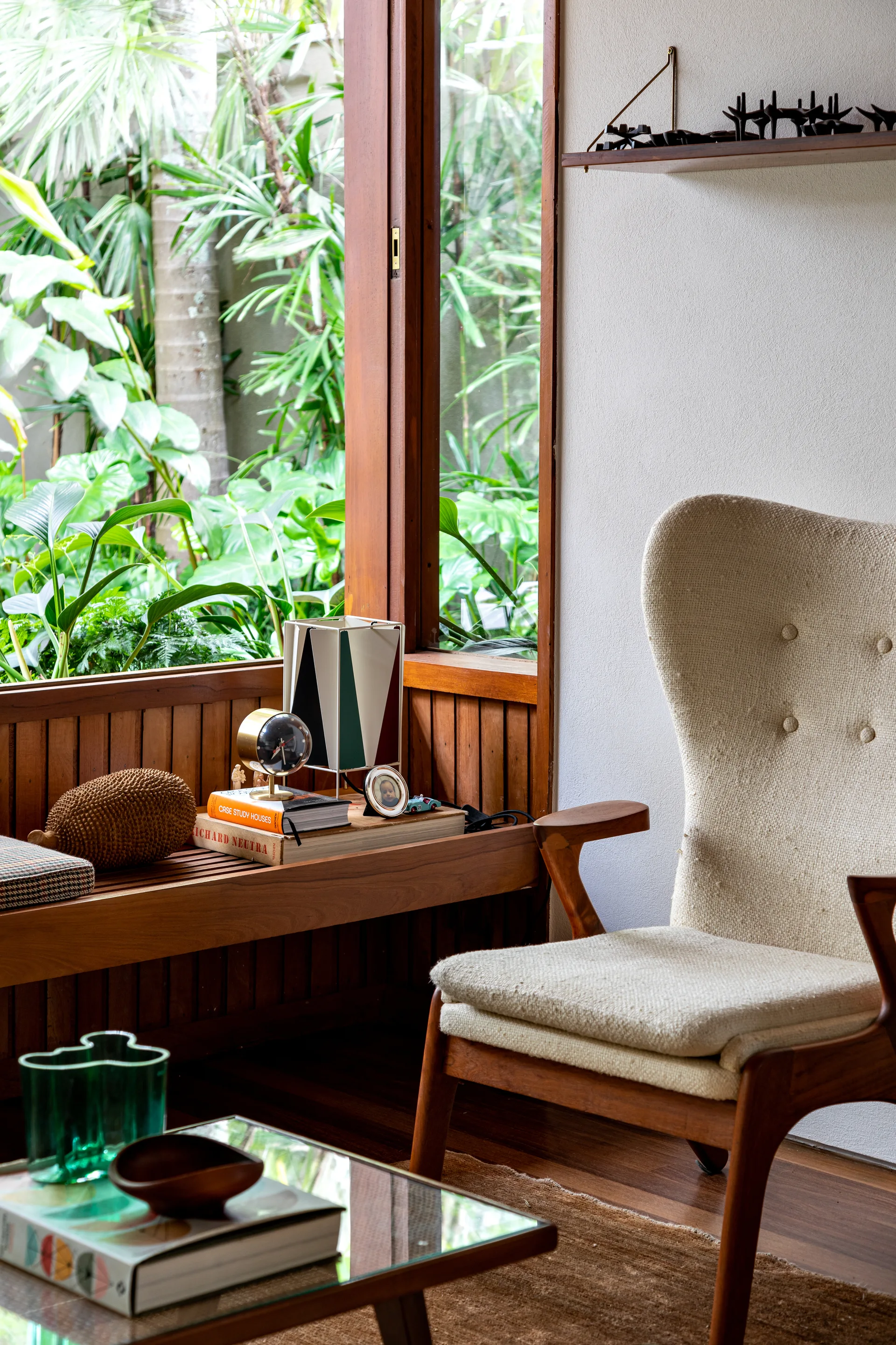 A textured cream armchair sits next to a wooden window bench overlooking a lush green tropical garden.