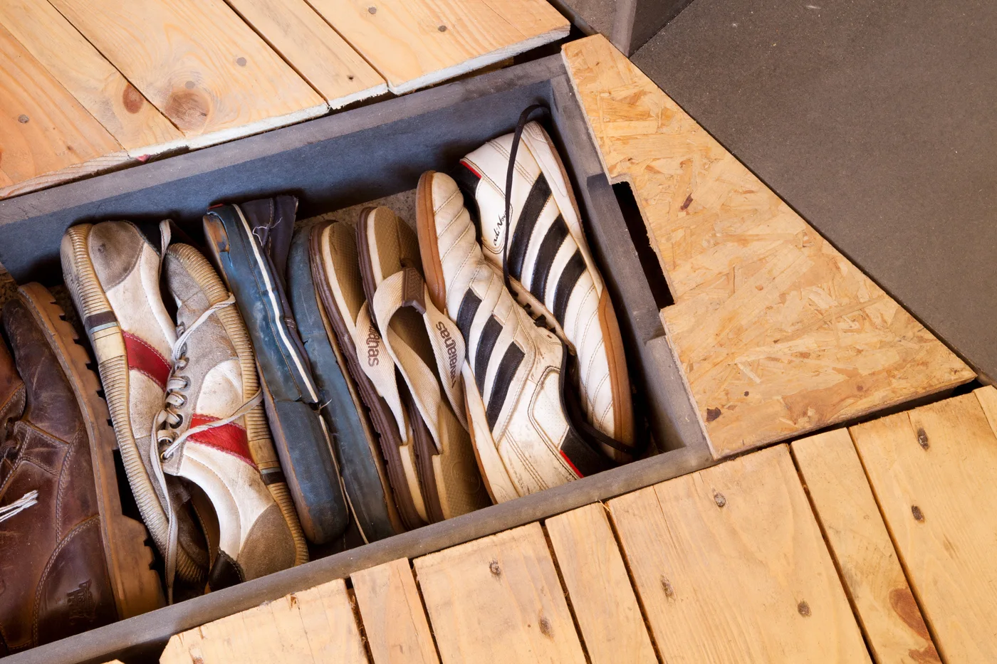 A top-down view of a recessed floor storage compartment filled with shoes, built into a light wood plank floor.