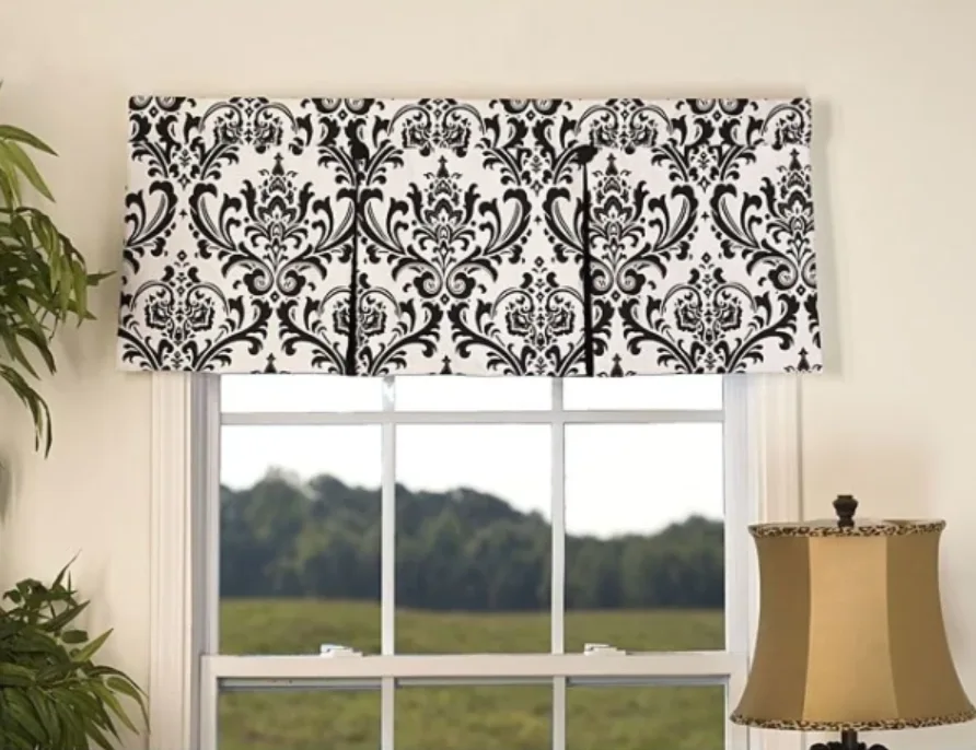 A black and white damask-patterned window valance is mounted above a white grid-frame window with green trees visible outside.