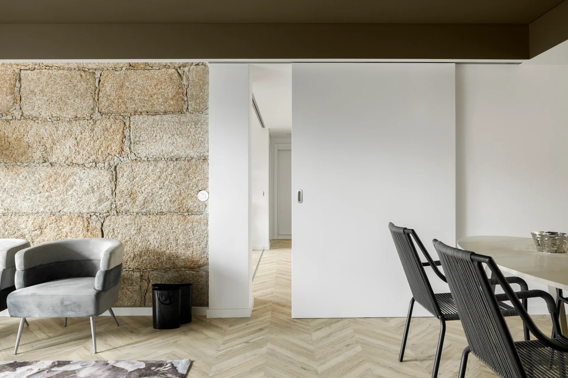 A modern room featuring a rustic stone block wall adjacent to a large white sliding door with chevron wood flooring.
