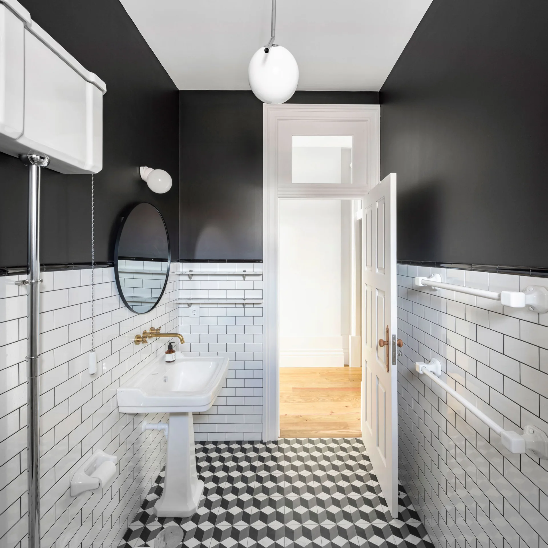 A small bathroom with white subway tile walls, a pedestal sink, black painted upper walls, and a black and white geometric tiled floor.
