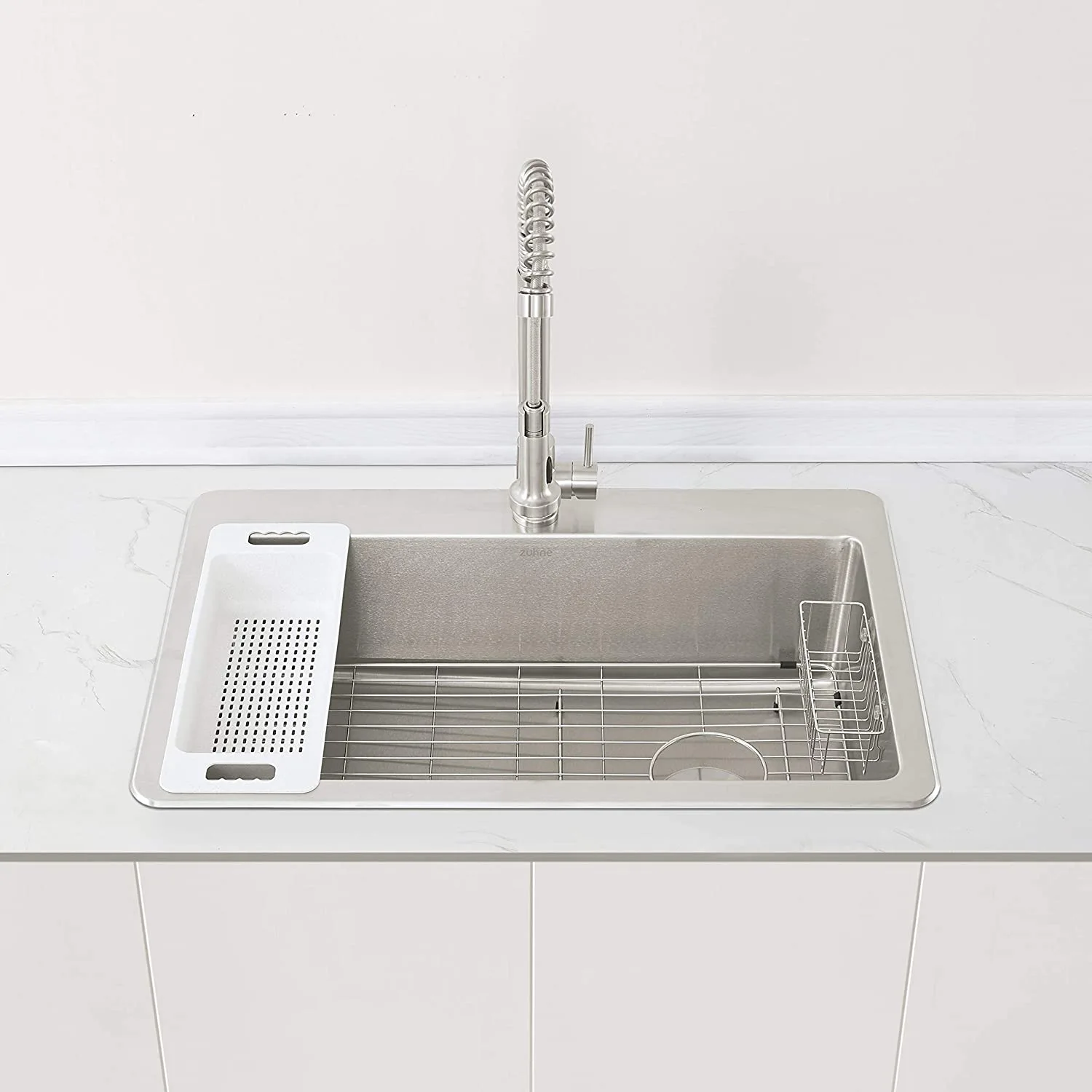 A stainless steel undermount kitchen sink in a white marbled countertop features a tall pull-down coil faucet, colander insert, and bottom grid.