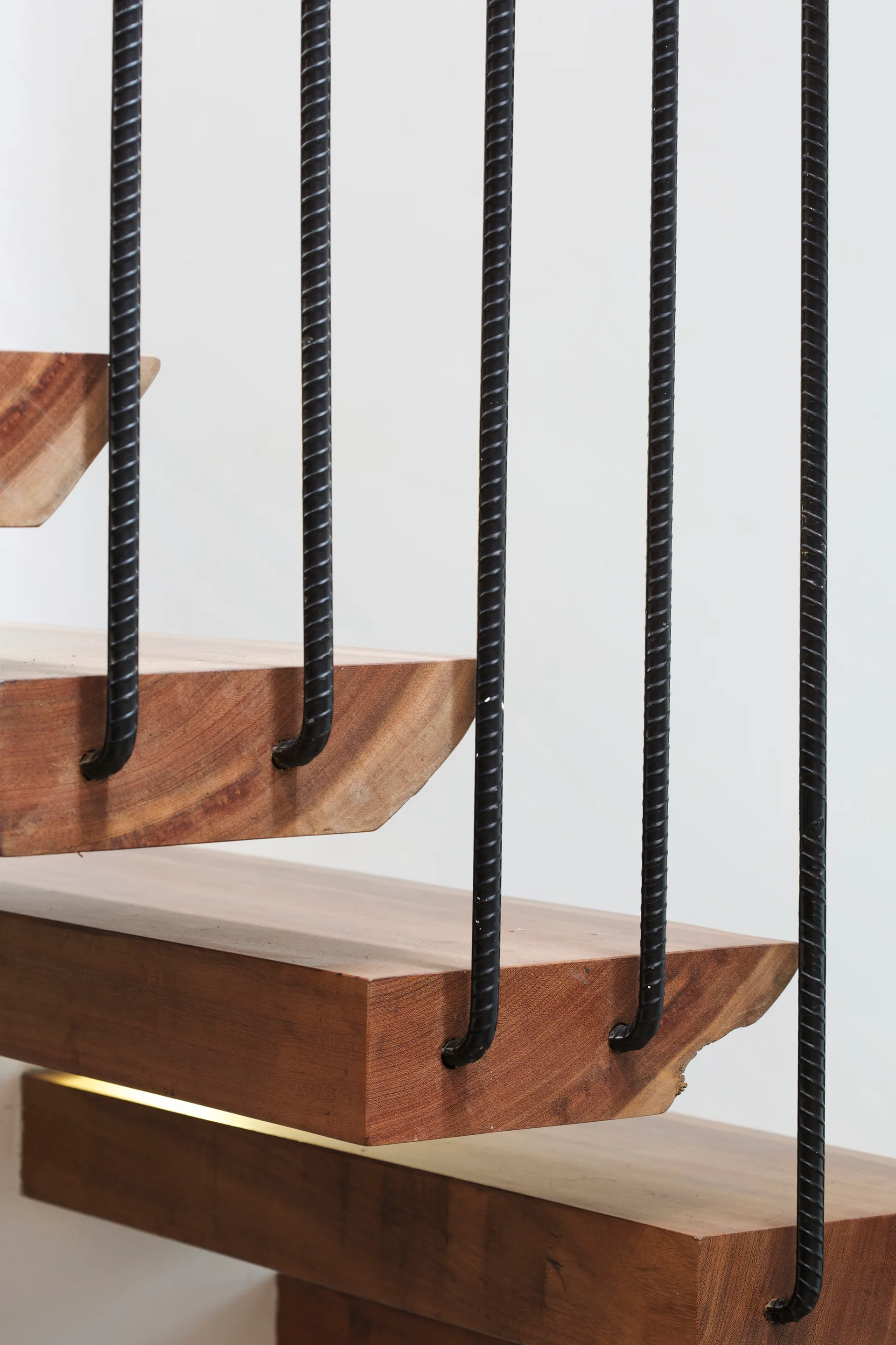 Close-up of floating wooden stair treads paired with vertical black steel rebar balustrades against a white wall.