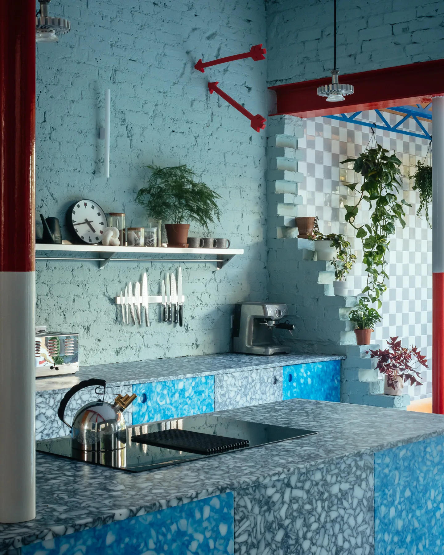 An industrial kitchen features a blue painted brick wall, speckled blue countertops and island, and a red structural support beam.
