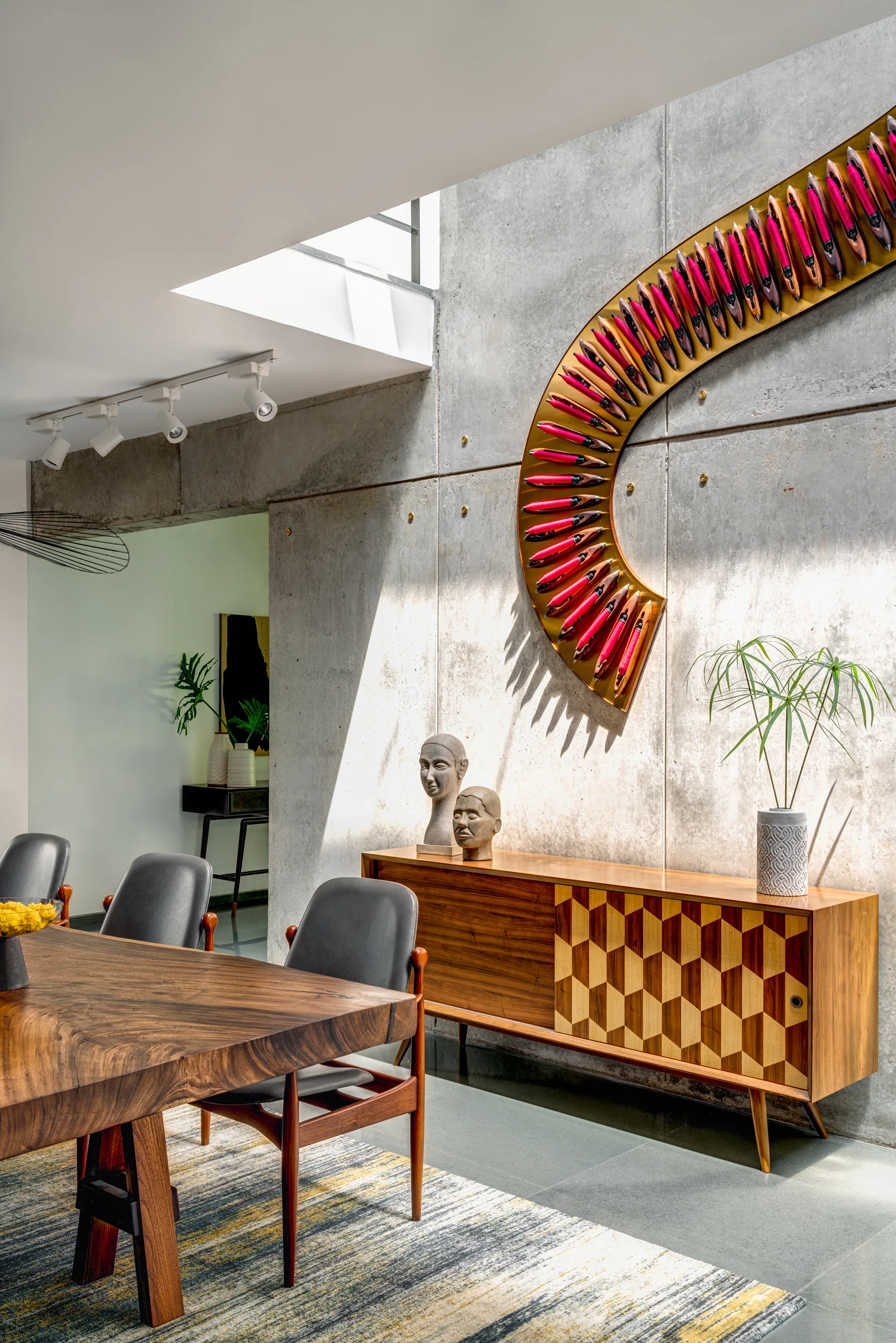 A modern dining room features a textured concrete wall, a wooden sideboard with geometric inlay doors, and a large curved decorative wall sculpture.
