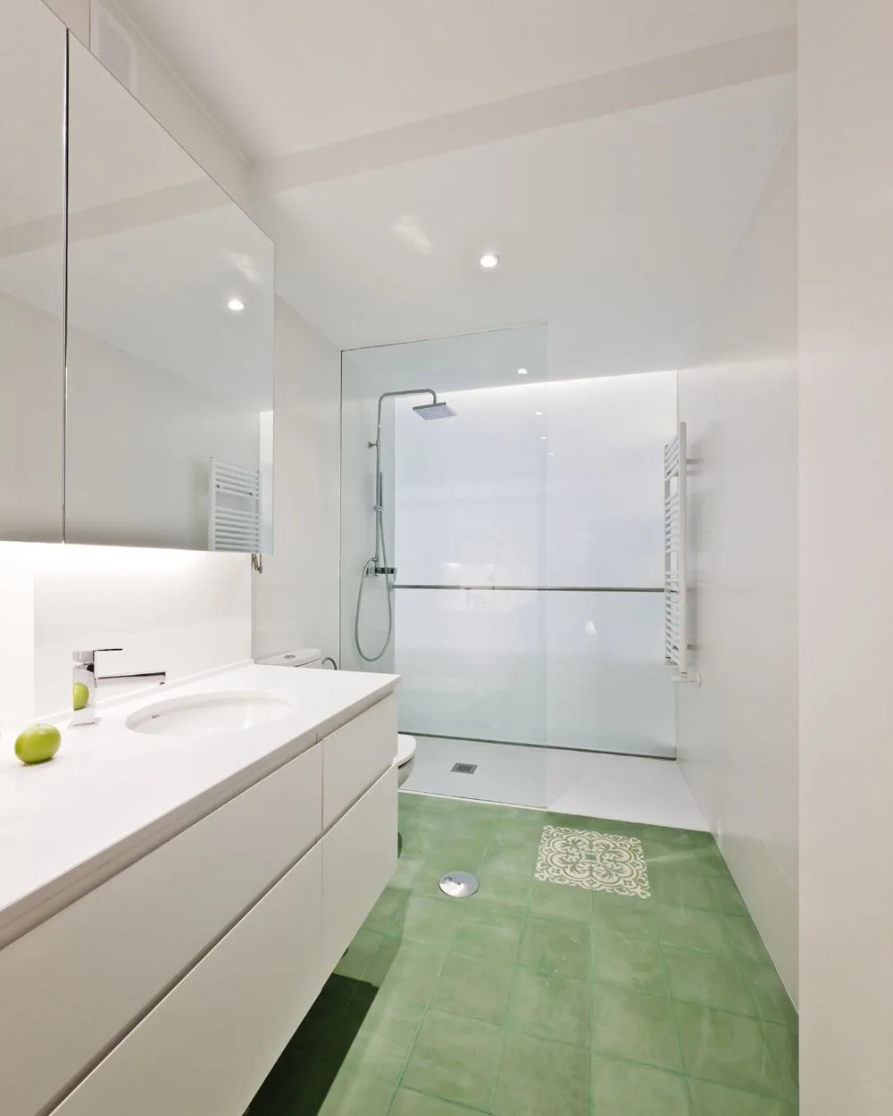 A modern white bathroom featuring a floating vanity with a round sink, a glass-enclosed shower, and a green tiled floor.