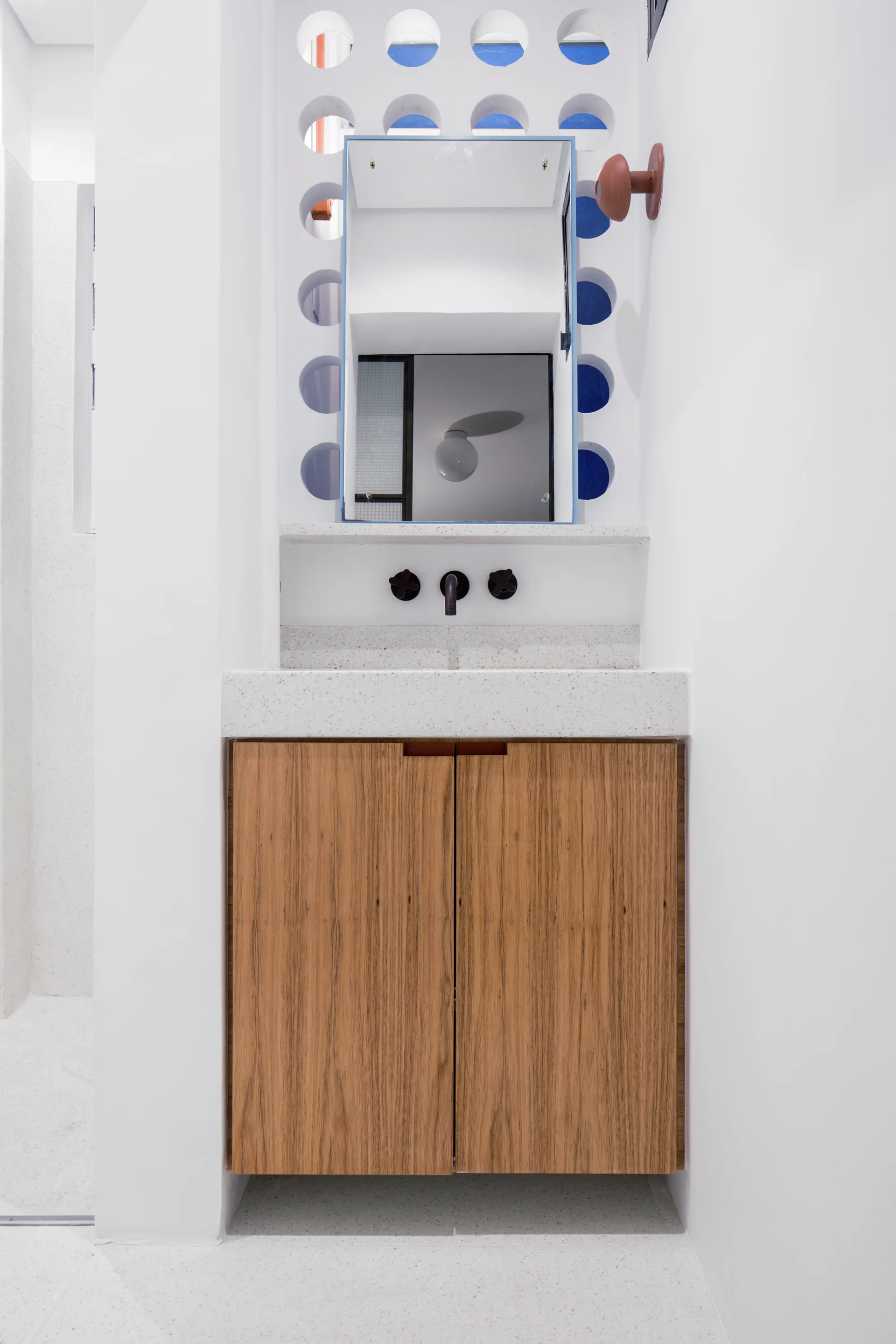 A modern bathroom vanity features a wood-toned cabinet, a white speckled countertop, and a decorative breeze block wall backdrop with circular cutouts.