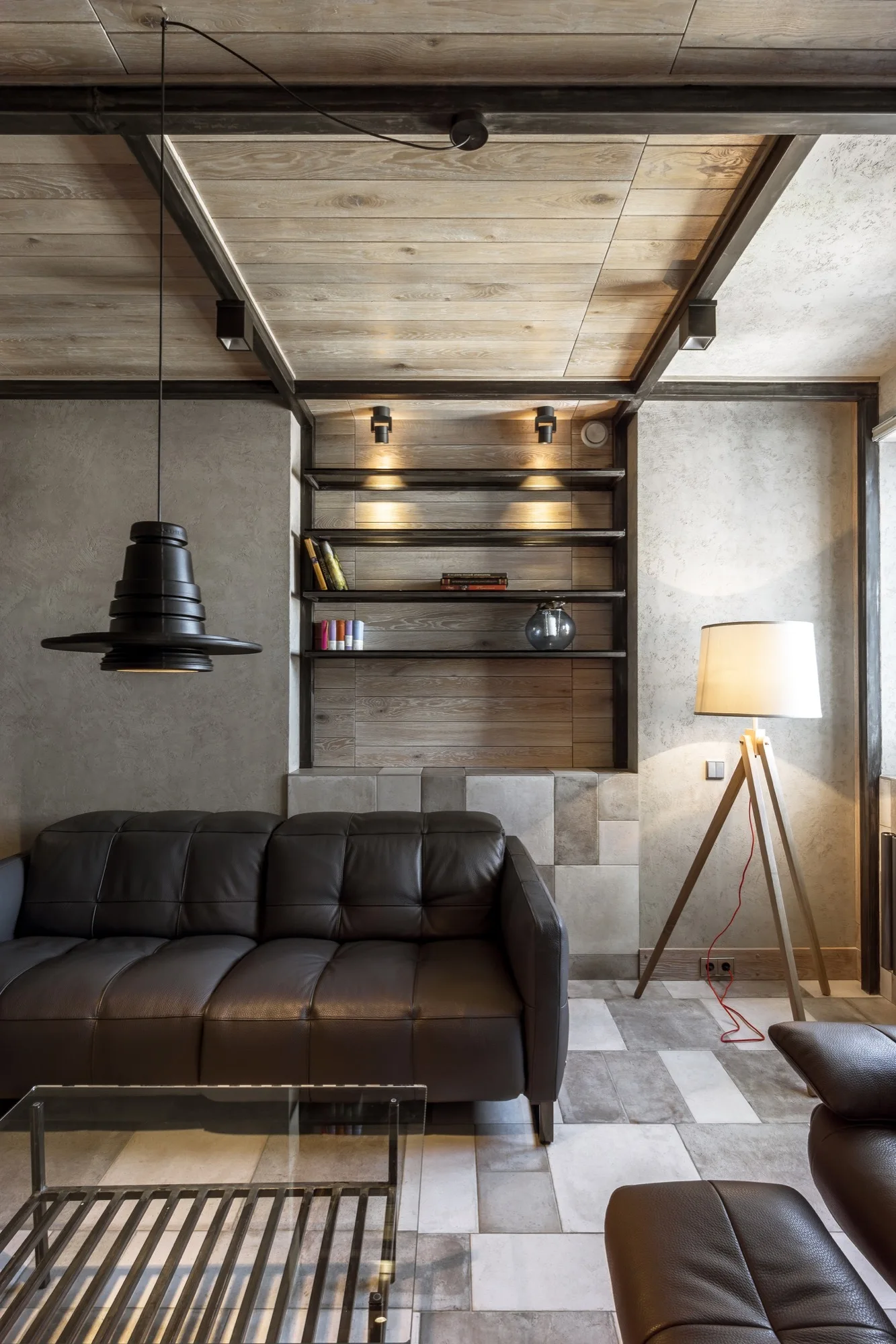 A modern industrial living room features a dark leather sofa, wood plank ceiling with metal beams, and a tripod floor lamp.