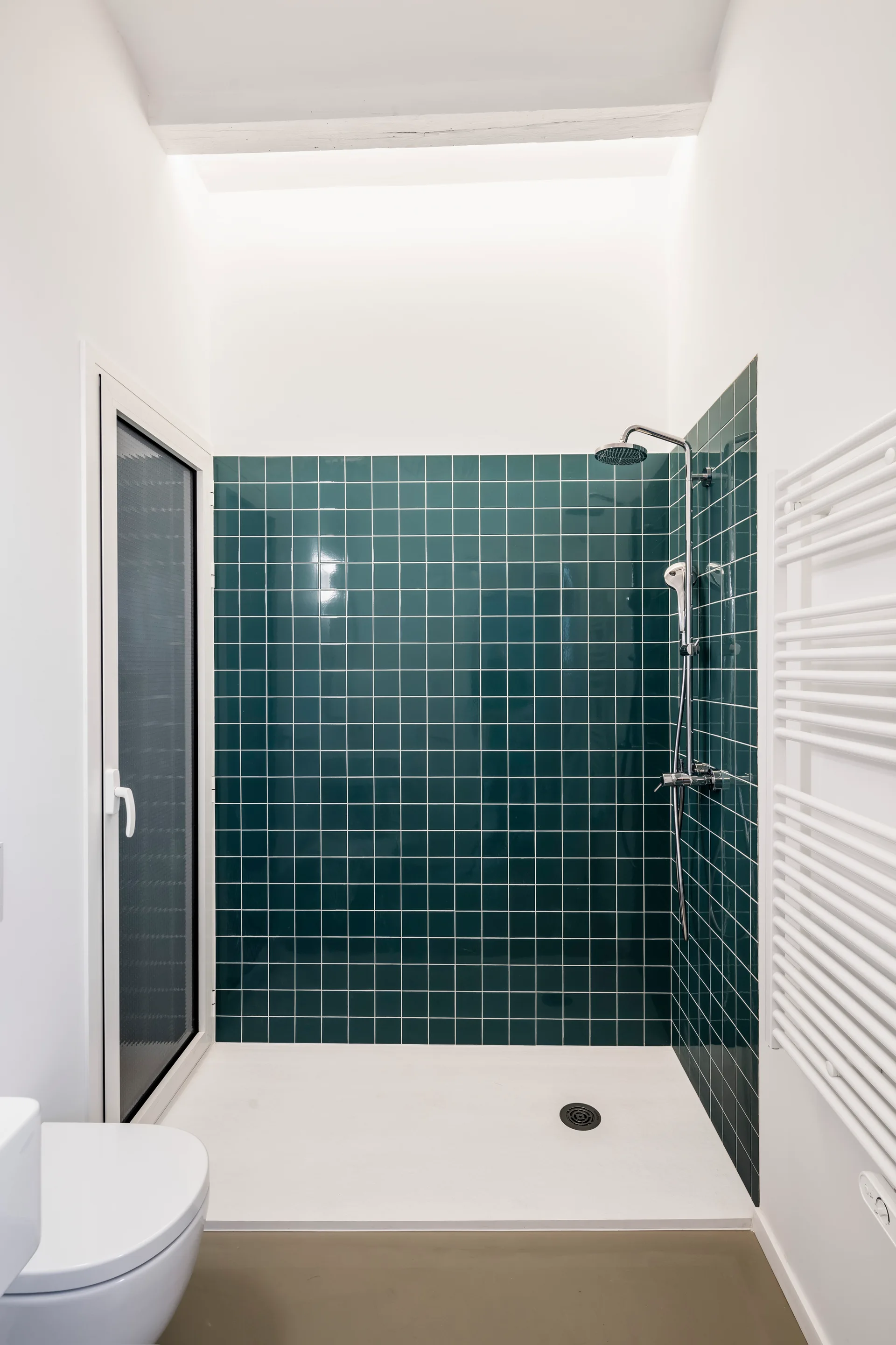 A modern shower stall features dark green square wall tiles, chrome fixtures, a white shower pan, and a white wall-mounted towel radiator.