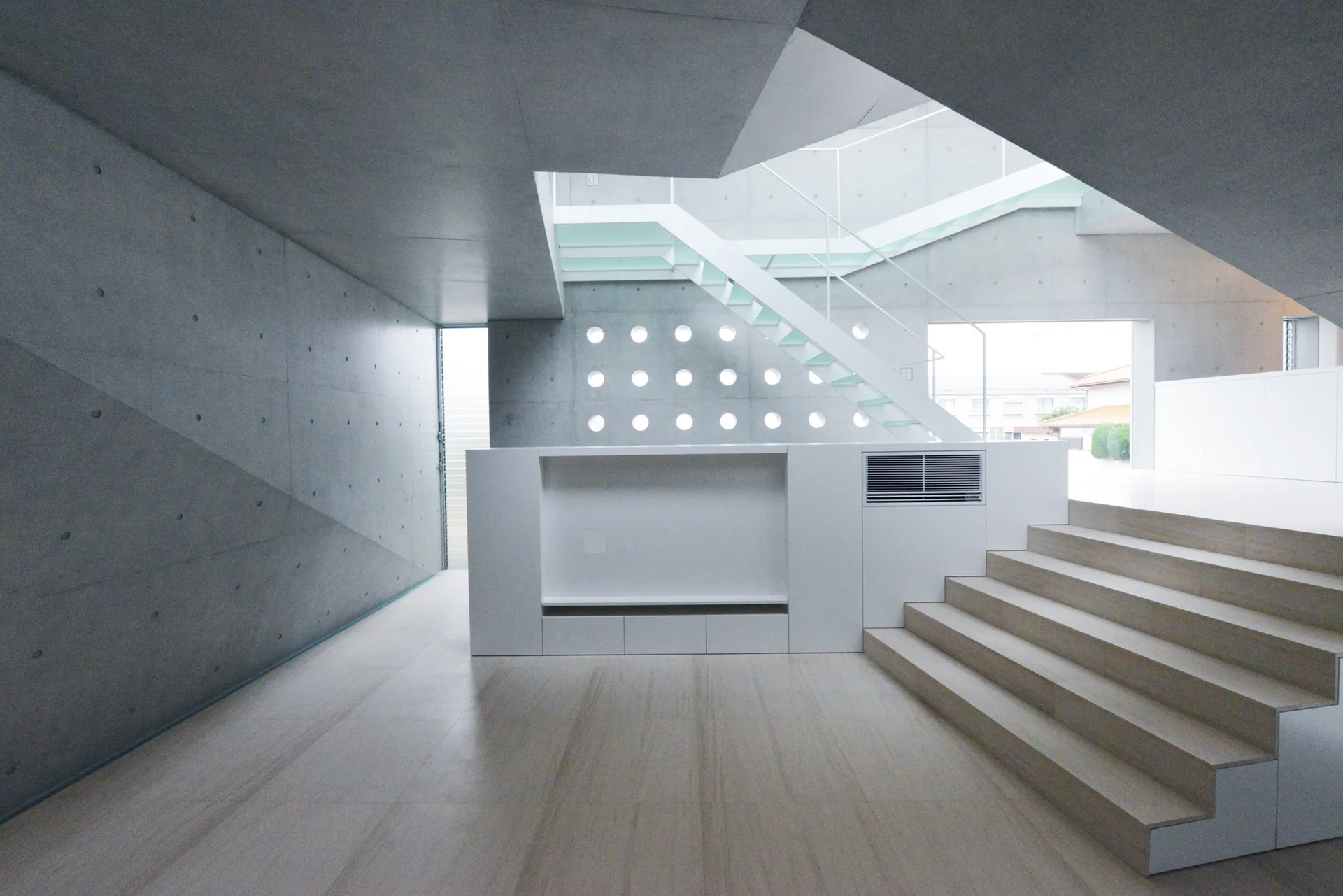 A minimalist room with raw grey concrete walls, light wood flooring, a low white cabinet, and a white open-riser staircase.