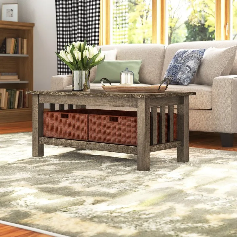 A rustic wood coffee table with two woven storage baskets underneath sits on a patterned rug in front of a beige sofa.