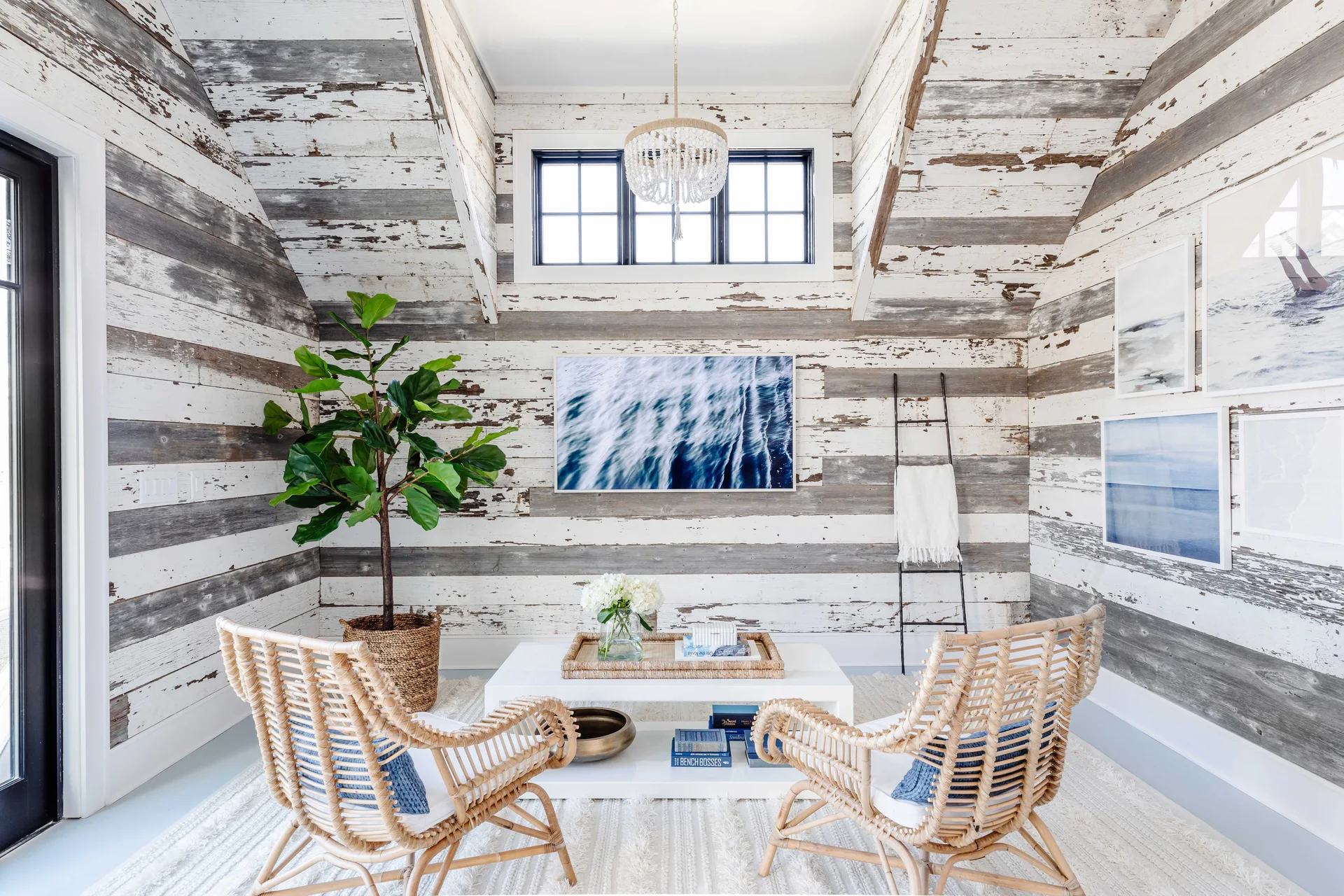A bright living area features distressed wood plank walls, sloped ceilings, two woven rattan armchairs, and a white coffee table.
