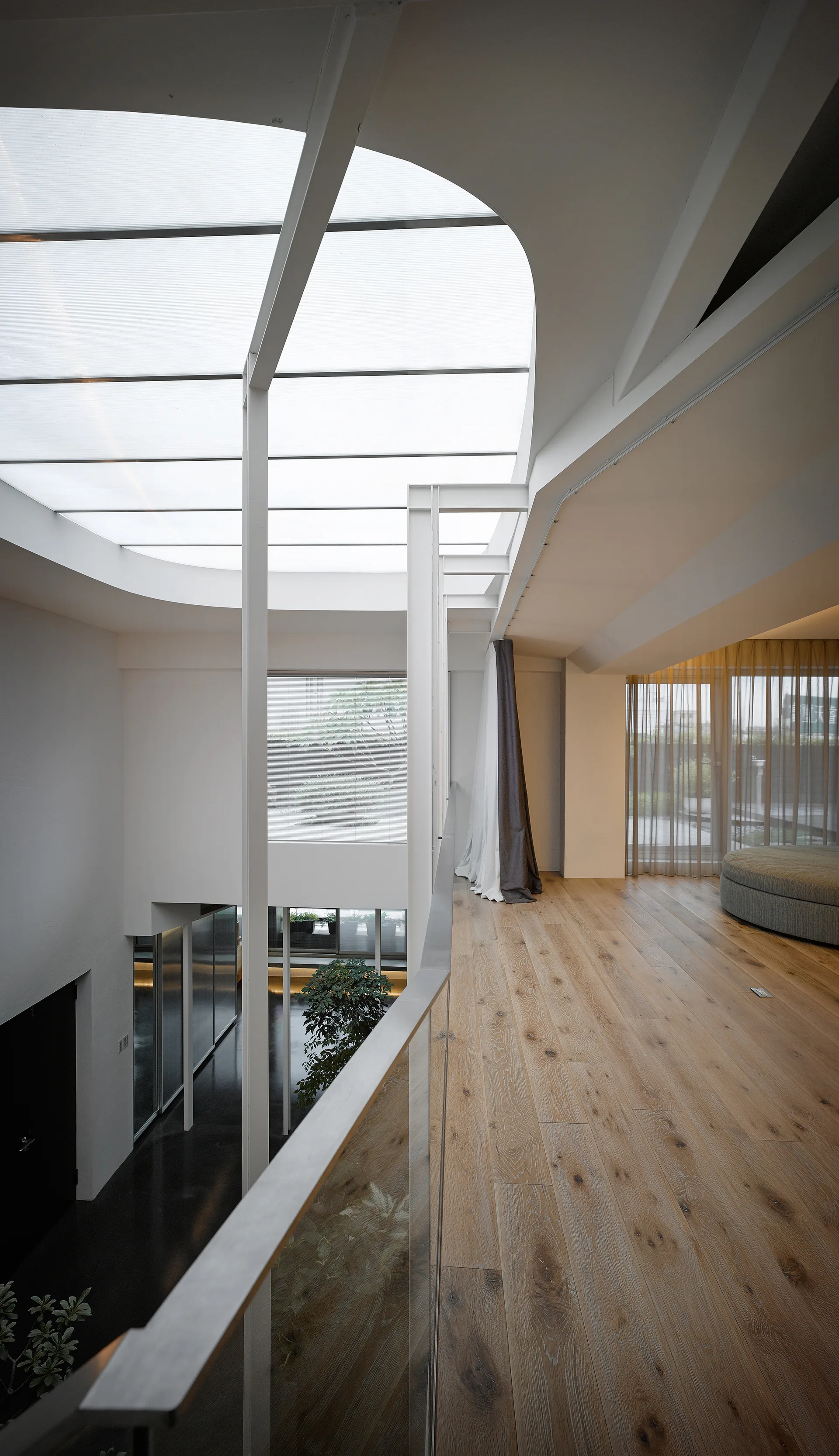 A modern wood-floored landing features a glass railing overlooking an open atrium under a large curved skylight.