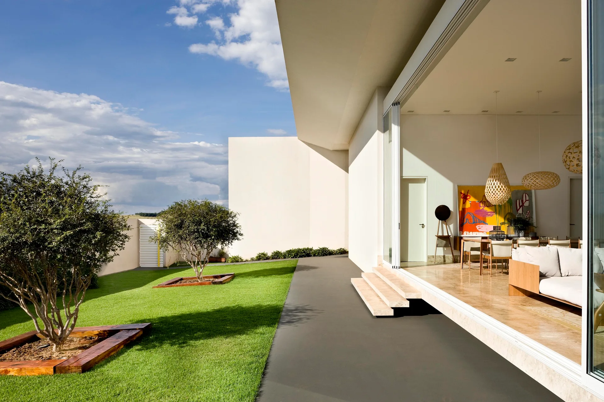 A contemporary living room with stone flooring opens through sliding glass doors to a manicured lawn with small trees.
