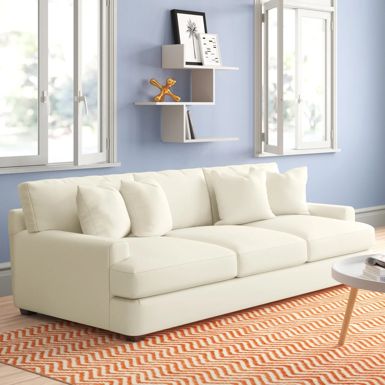 A plush white sofa sits on an orange zigzag rug in front of a light blue wall with two open windows and a geometric shelf.