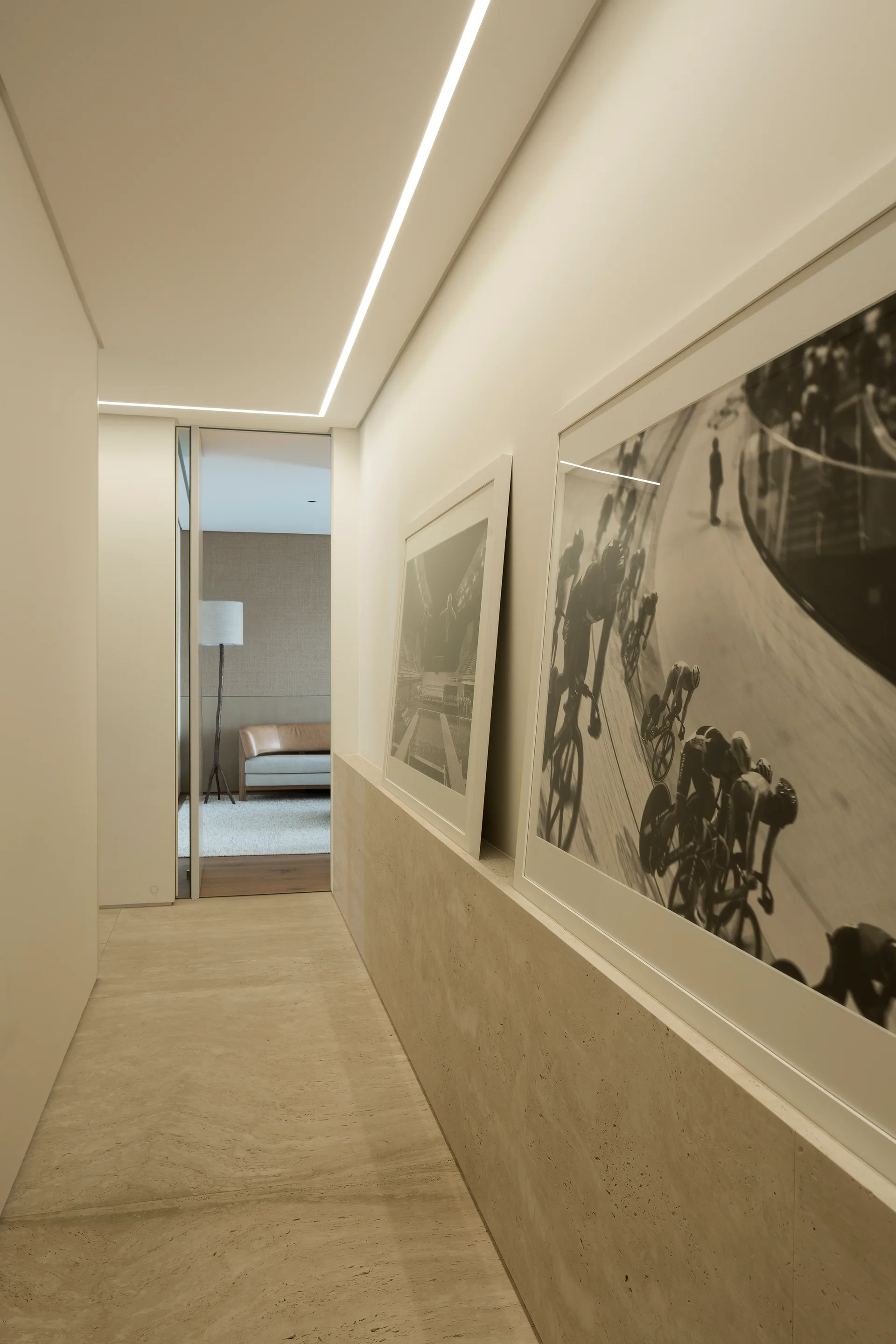 A modern neutral hallway features a built-in stone ledge supporting framed photographs beneath a linear ceiling light strip.