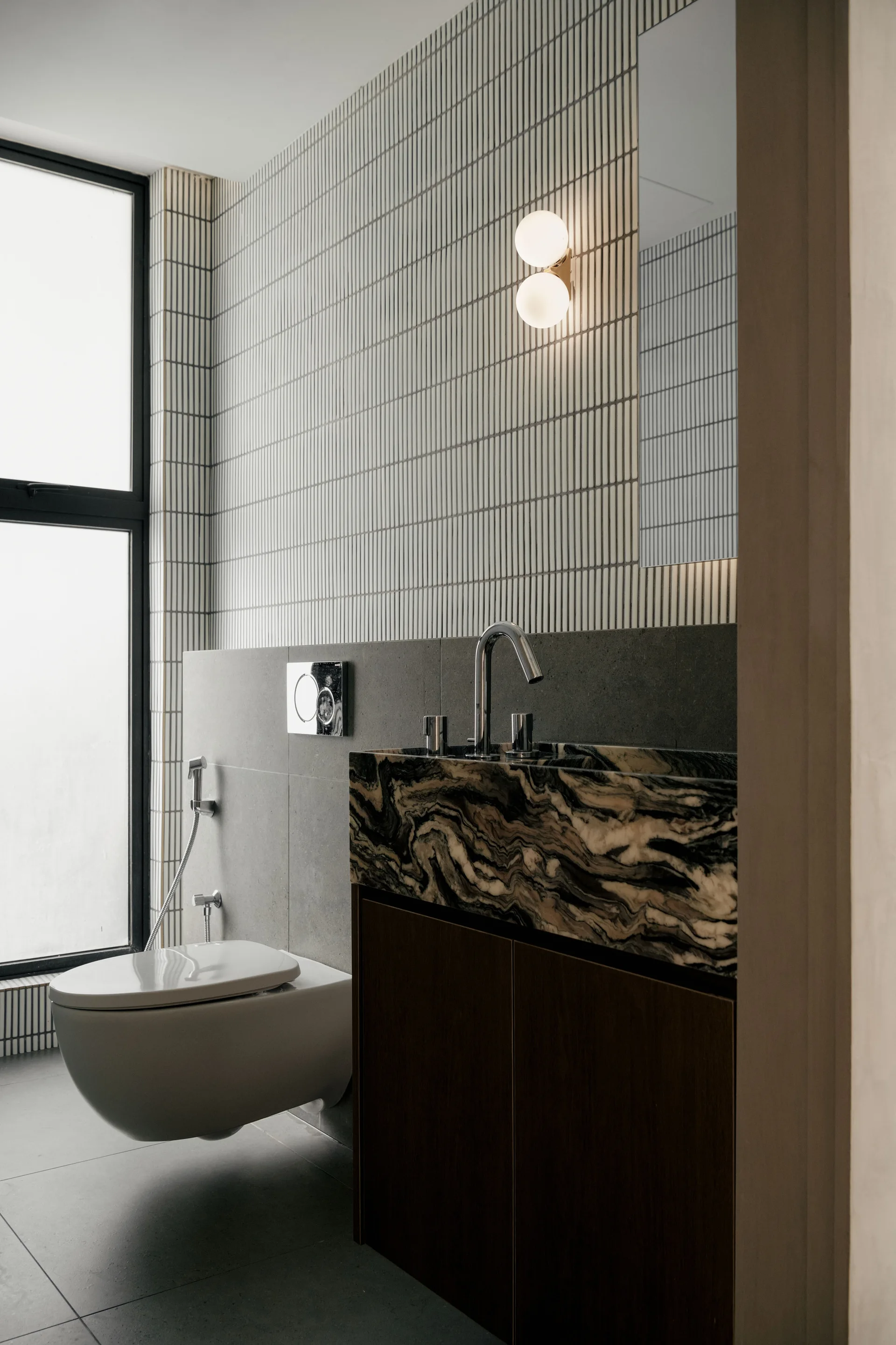 A modern bathroom featuring a heavily veined marble vanity sink, a wall-mounted toilet, and walls clad in textured vertical linear tiles.