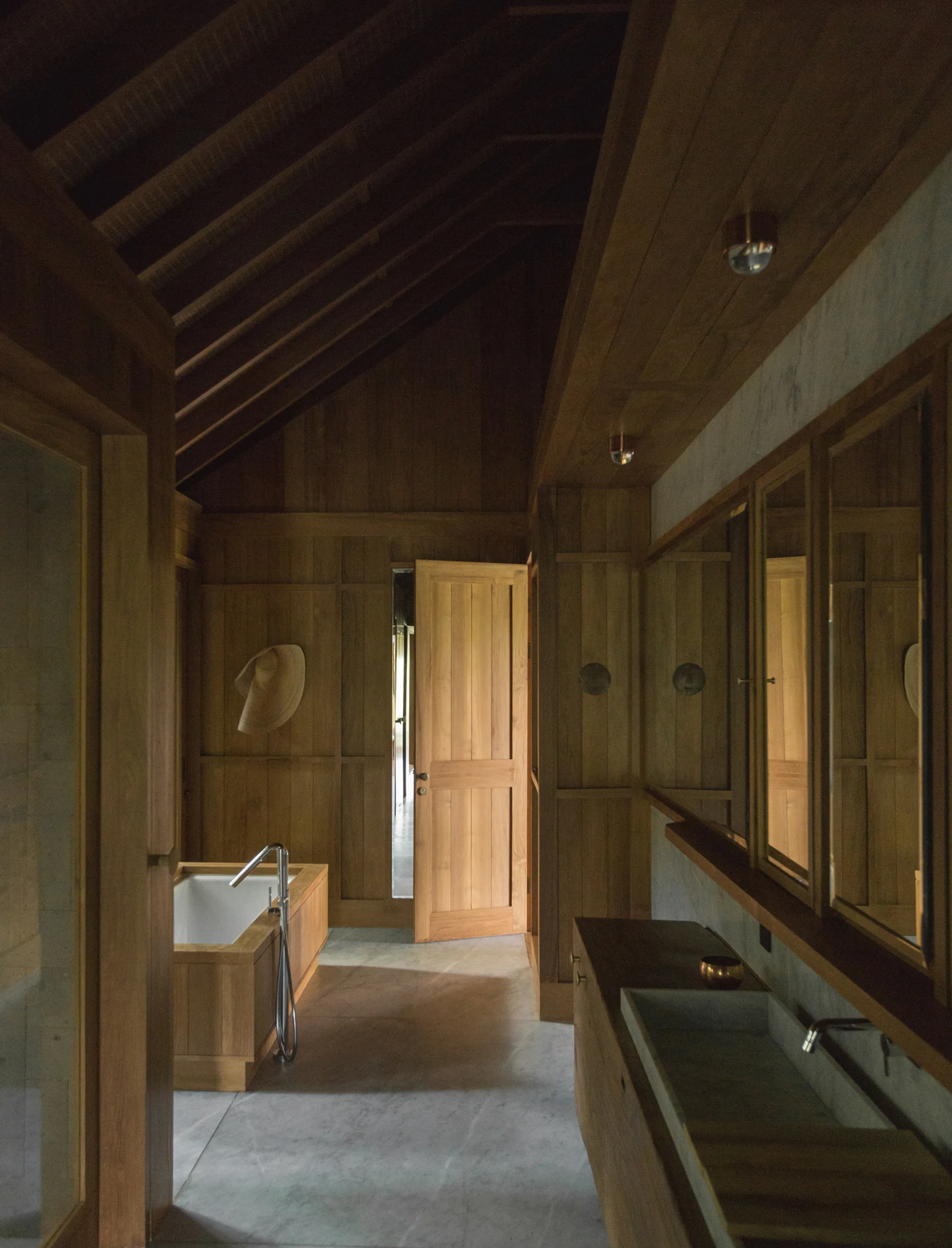 A wooden bathroom featuring a vaulted ceiling, a wood-framed bathtub, gray stone floors, and a long wooden vanity with a stone sink.