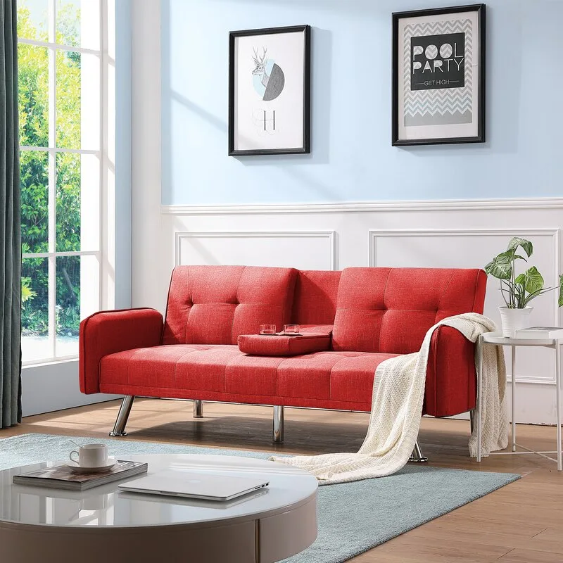 A modern red tufted sofa bed rests on wood flooring against a light blue wall with white wainscoting and black-framed art.