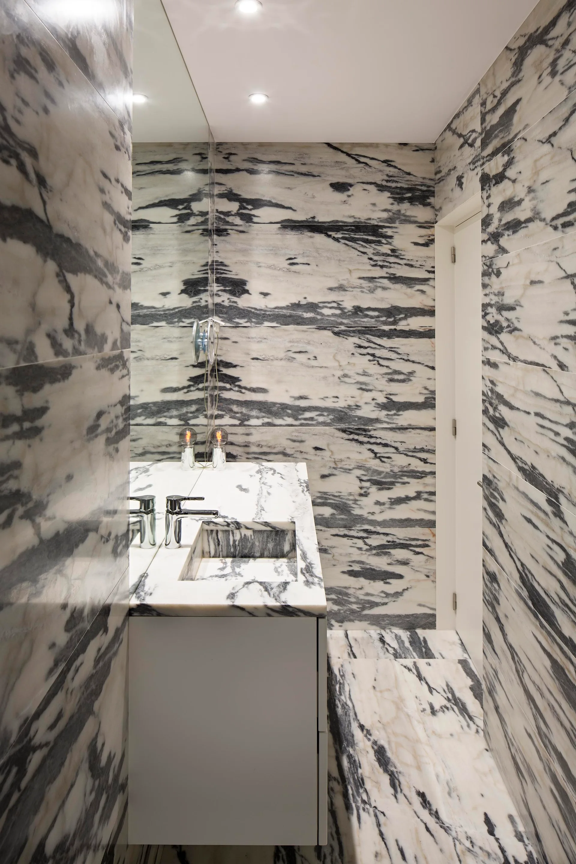 A contemporary powder room with walls and floor clad in heavily veined white and grey marble featuring an integrated stone sink vanity.