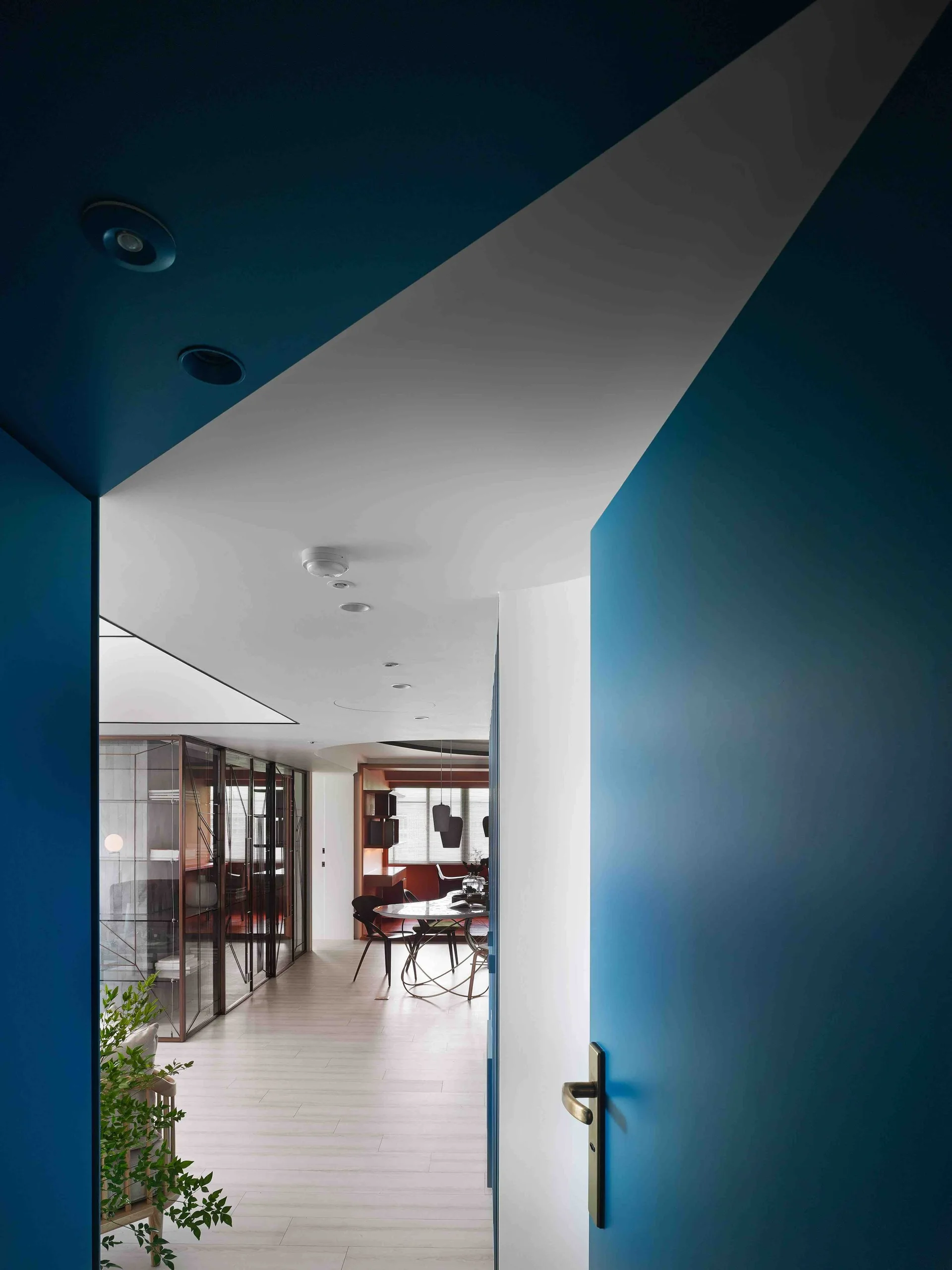 Looking through a matte blue painted doorway into a bright dining room with light wood floors, a glass cabinet, and an oval table.