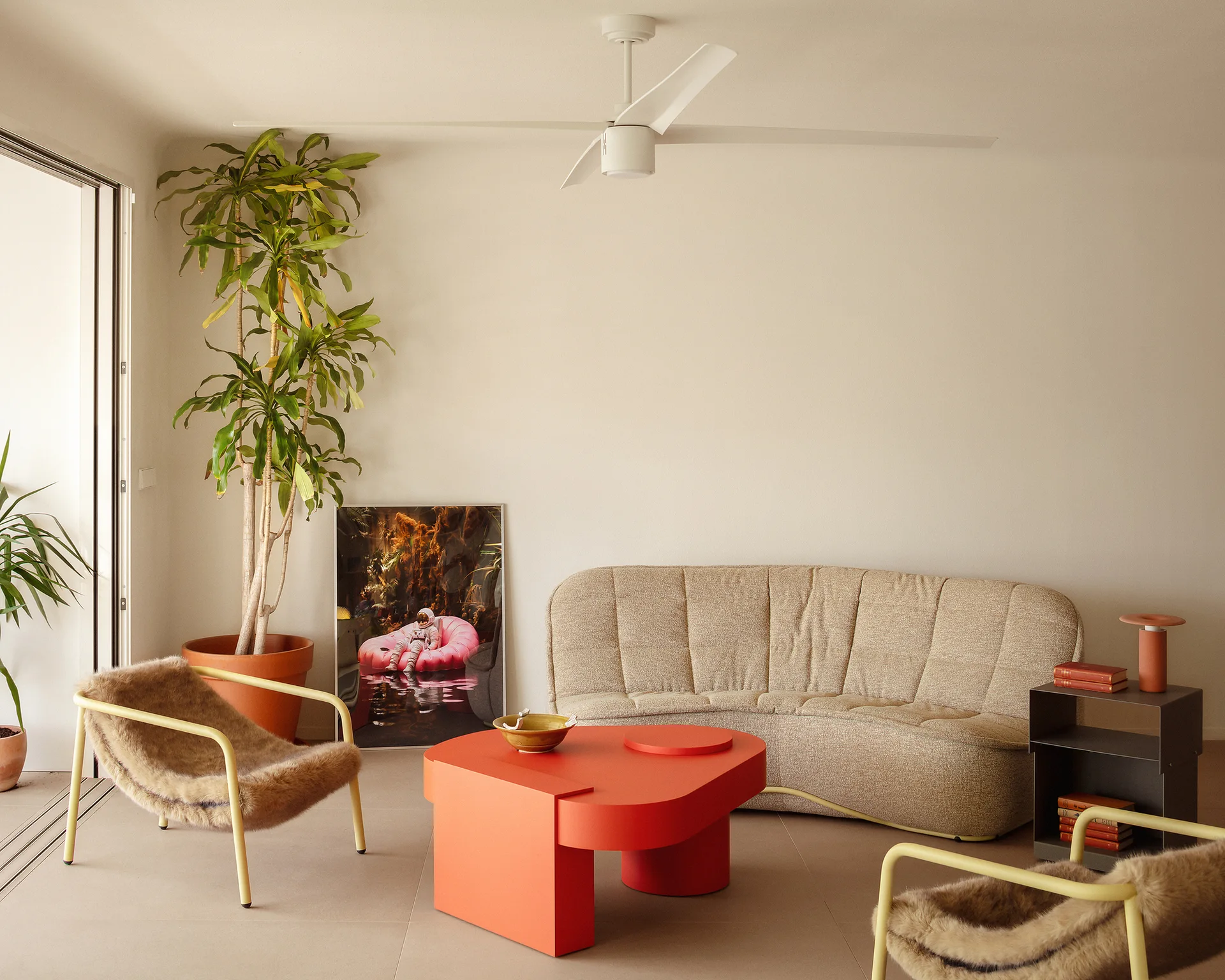 A modern living room features a curved beige sofa, a low orange geometric coffee table, and two yellow-framed armchairs with shaggy faux fur seats.