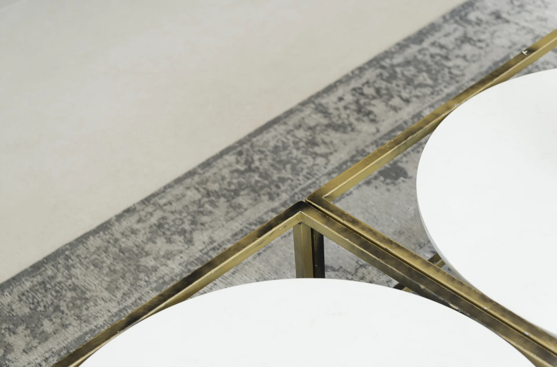 A close-up of nested coffee tables with circular white stone tops and square brass frames on a grey patterned rug.