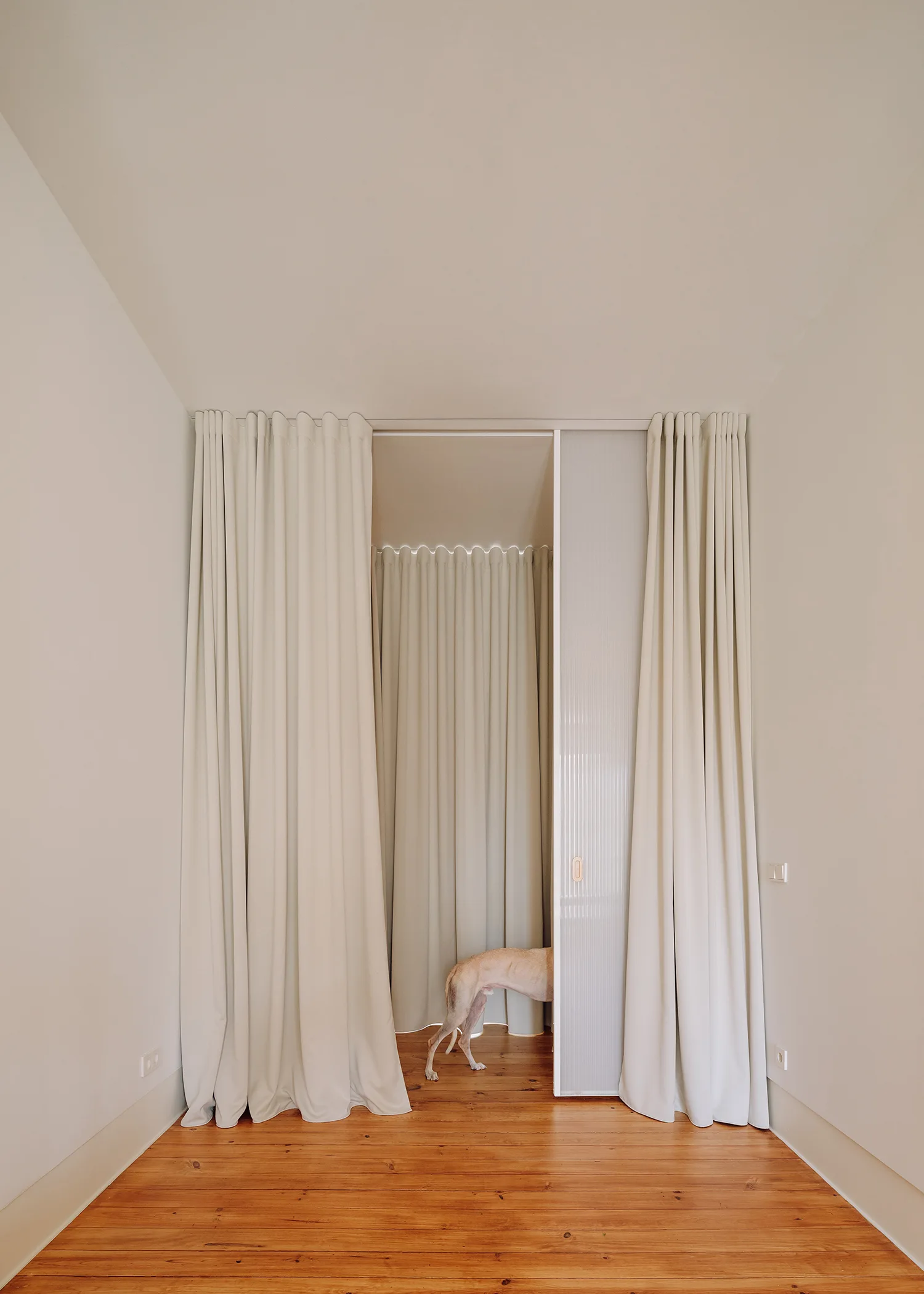 A minimalist doorway featuring cream-colored floor-to-ceiling curtains, a fluted glass sliding door, and warm wood plank flooring.