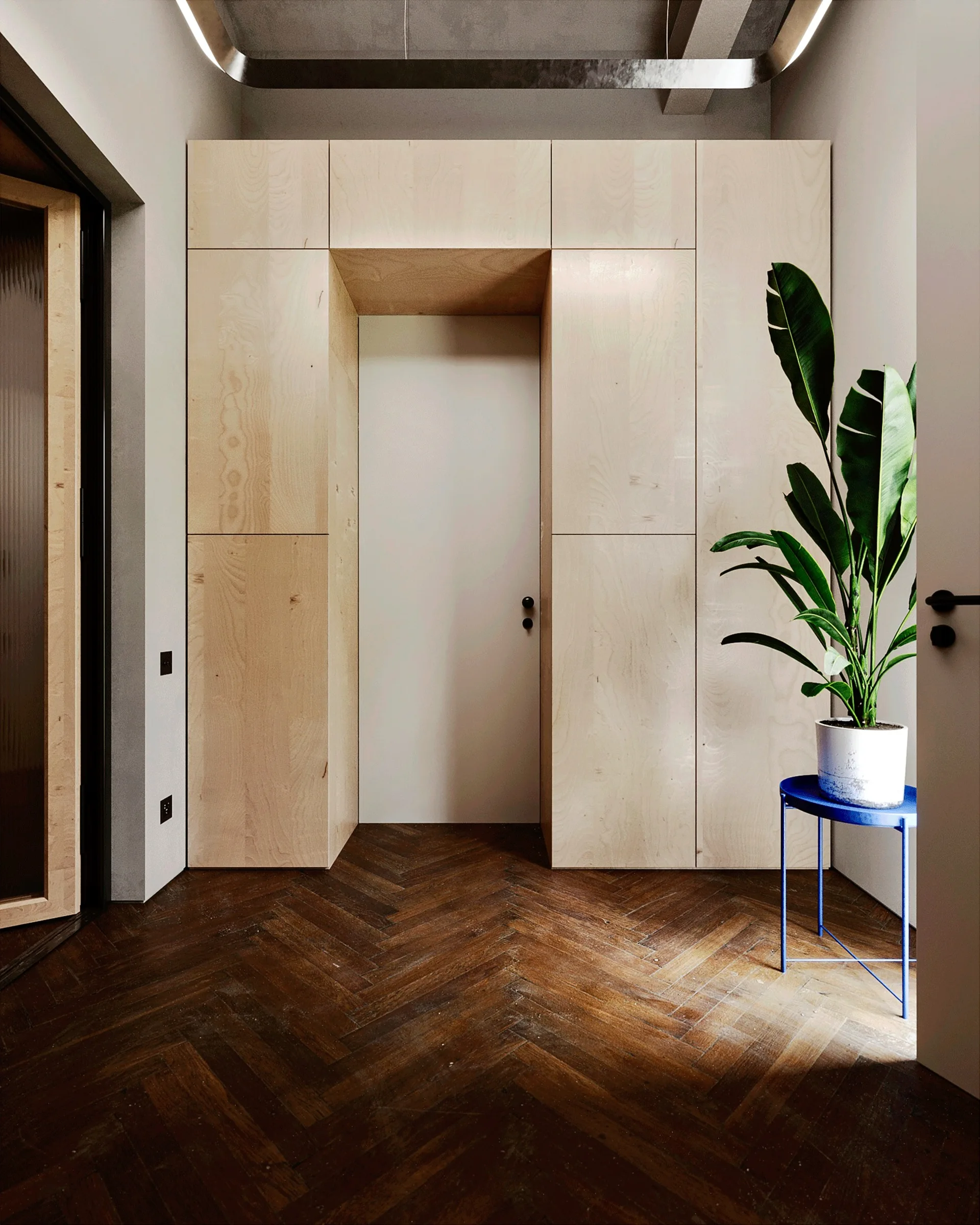 A modern entryway featuring light wood built-in cabinetry around a white door, dark wood herringbone flooring, and a potted plant on a blue stand.