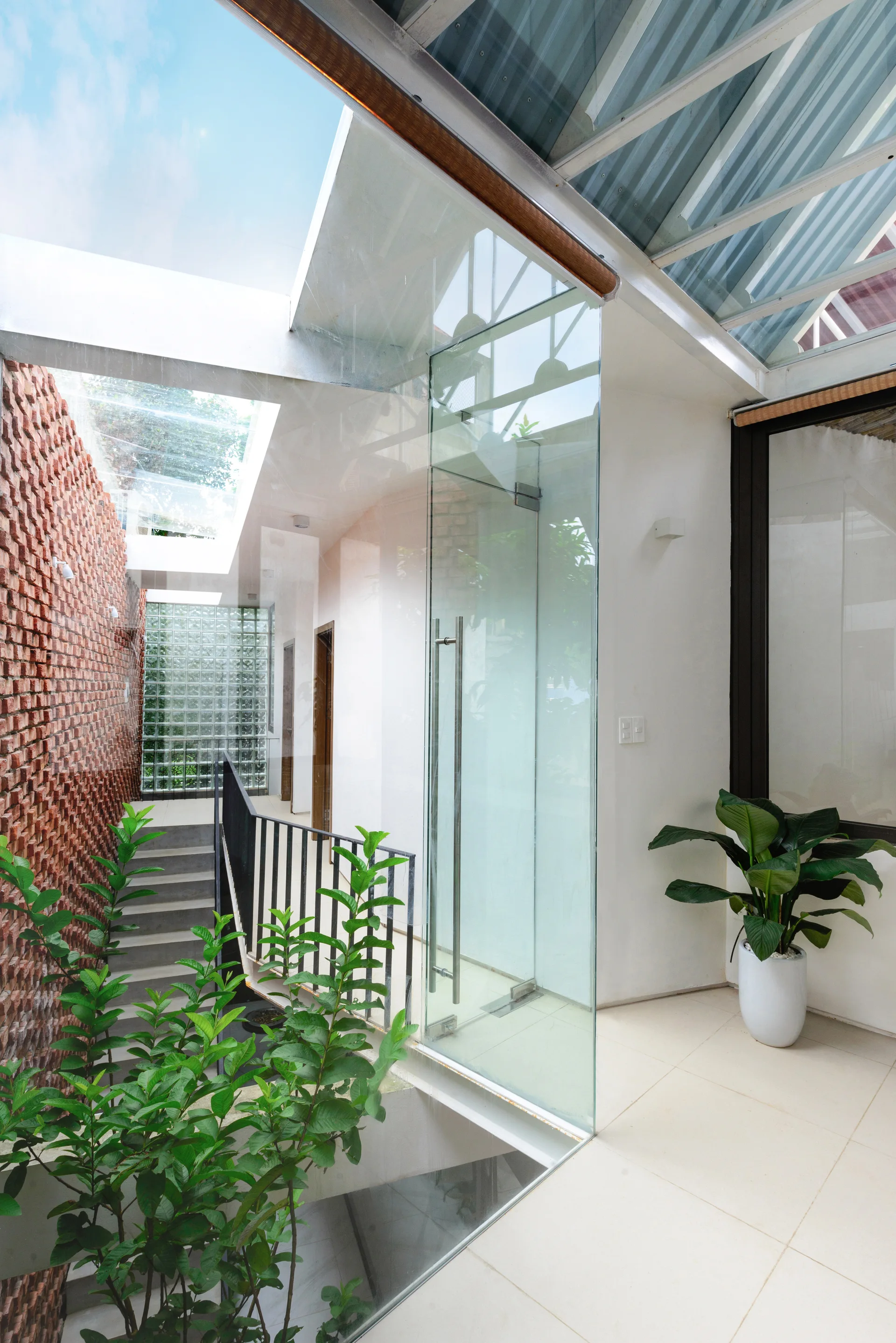 A bright indoor staircase landing features a textured red brick wall, a frameless glass partition, and a large overhead skylight.