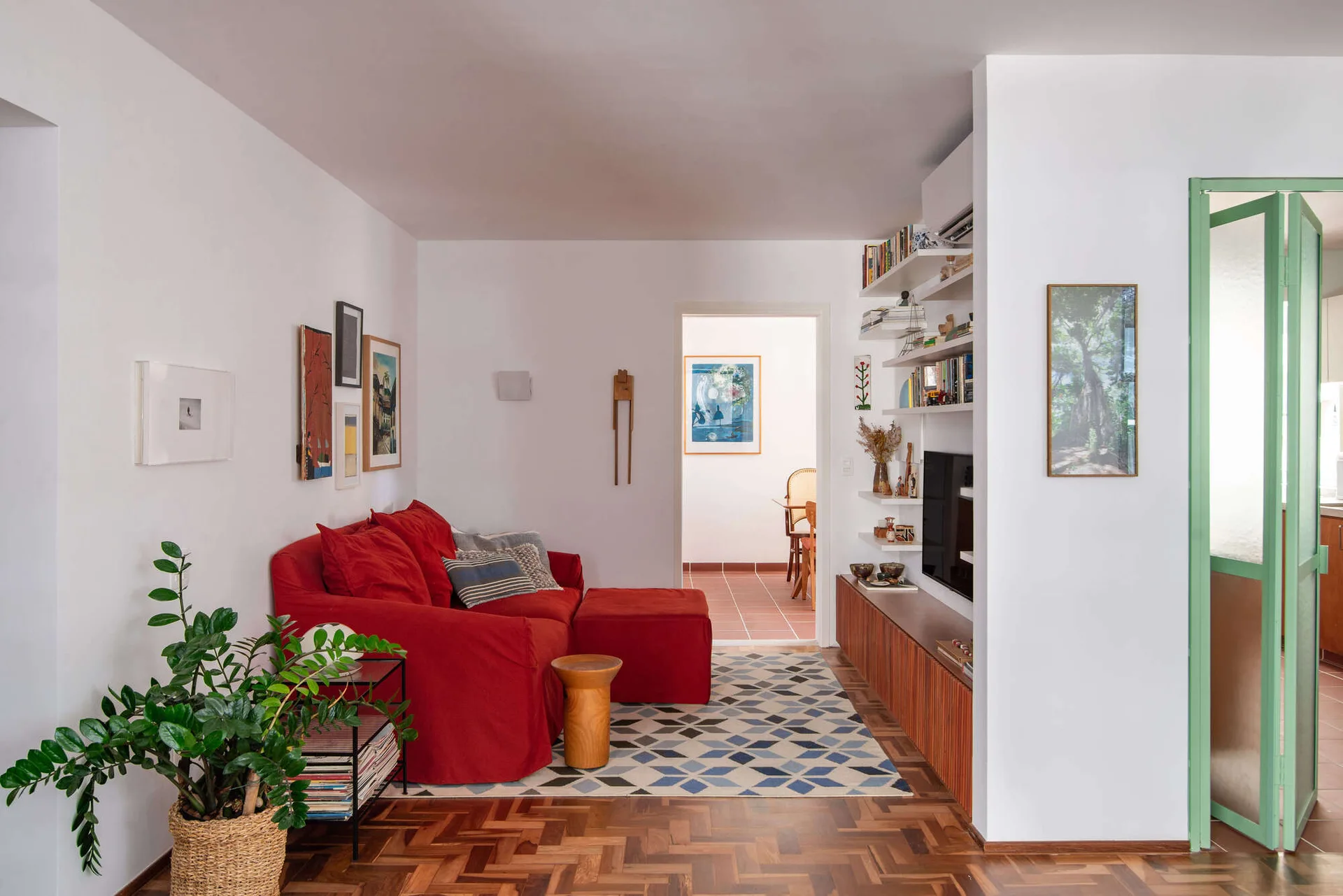 A living room featuring a red slipcovered sofa, a blue geometric rug, a slatted wood media console with open shelves, and parquet flooring.